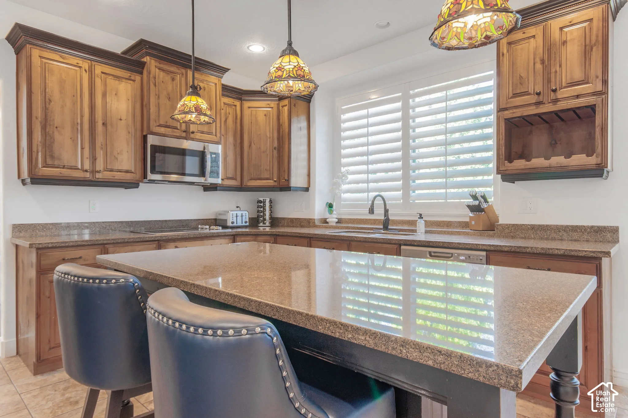 Kitchen featuring wood cabinetry, stone-surface countertops, center island, integrated sink with matte black faucet, and stained-glass pendant lighting