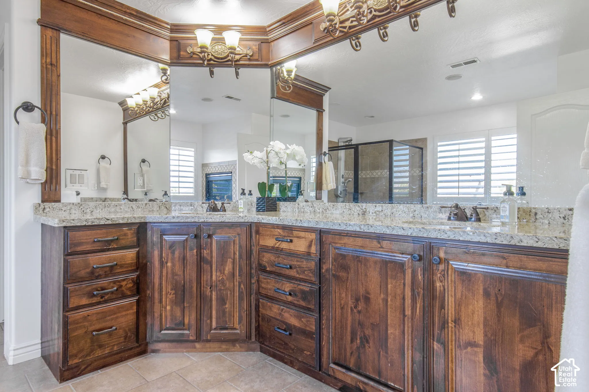 Custom wood cabinetry with extensive storage drawers, natural stone countertops, dual vanity sinks, ornate light fixtures, and expansive wall-to-wall mirrors