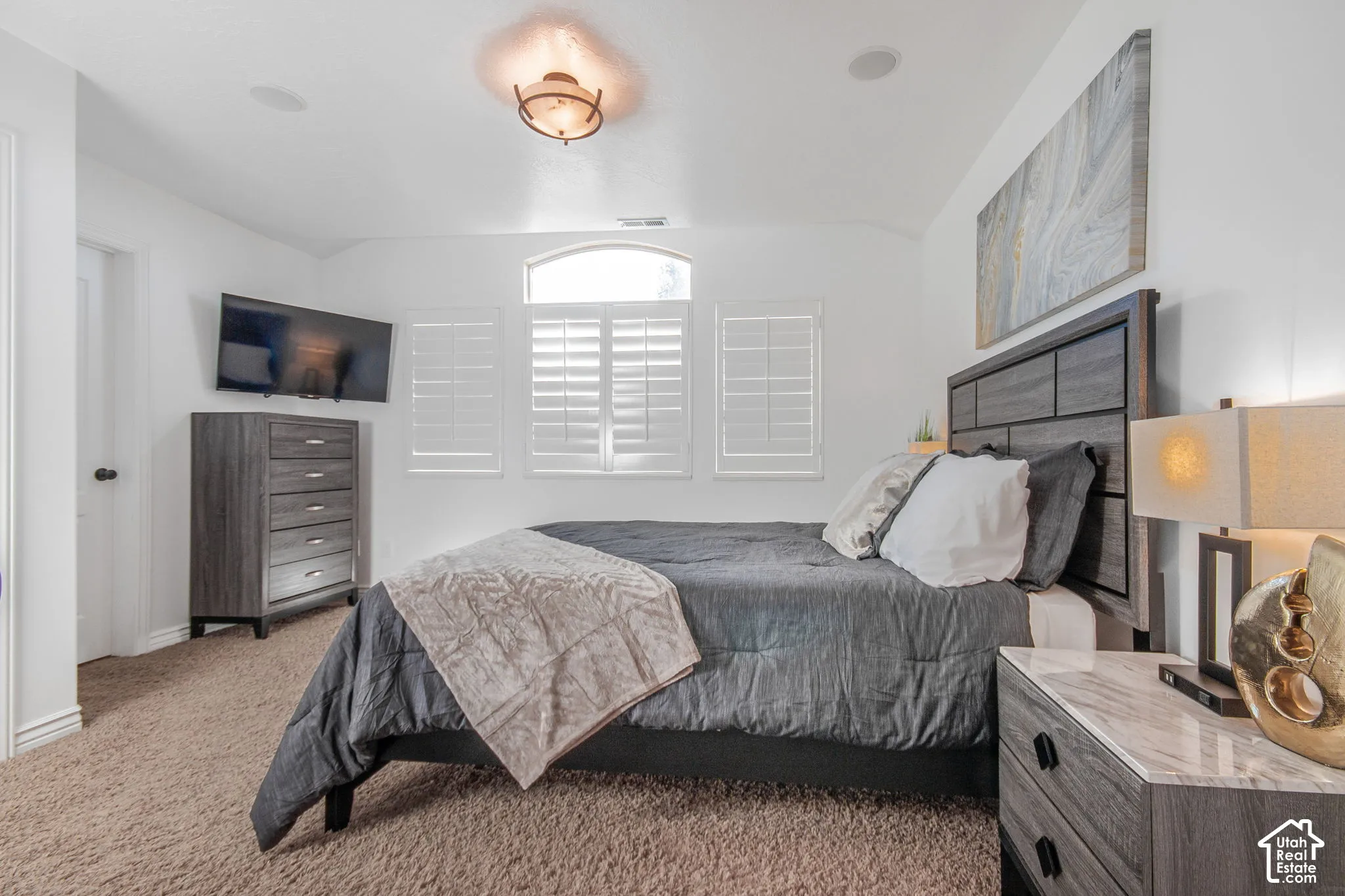 Neutral carpeted flooring, white plantation shutters, arched window detail, ceiling-mounted flush light fixture, and inset ceiling speakers