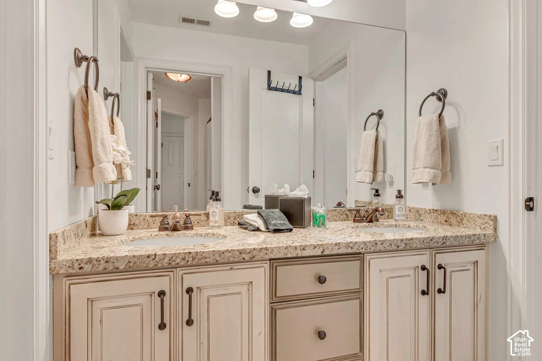 Dual-sink vanity with stone-finish countertop, undermount sinks, custom cabinetry, oil-rubbed bronze hardware, and oversized wall-to-wall vanity mirror