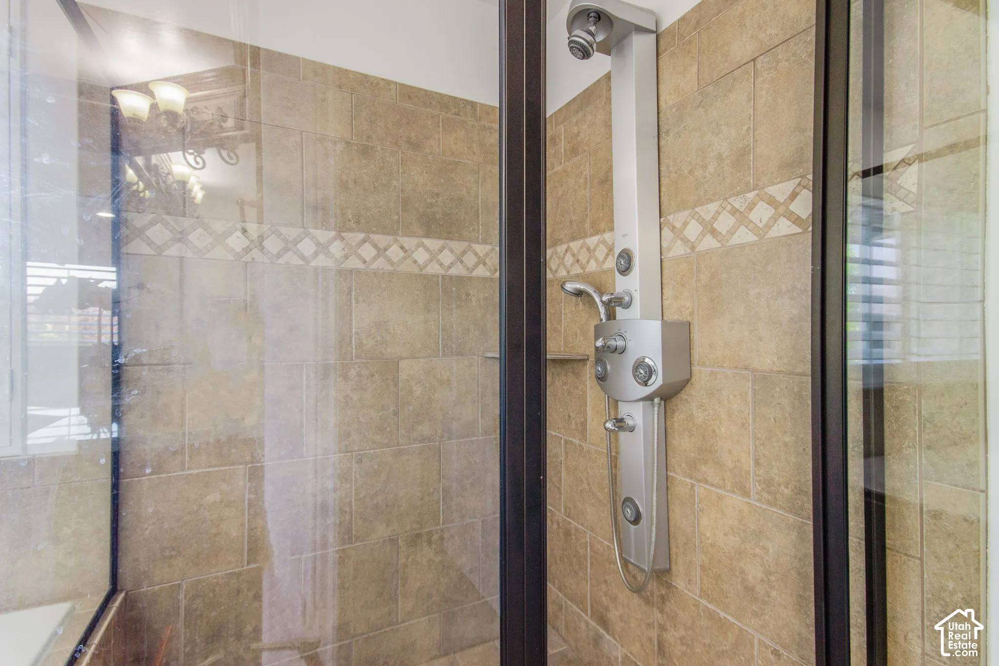 Shower enclosure featuring stone-tile wall surround with decorative accent inlay, integrated multi-head shower panel system, handheld shower attachment, and dark-finish metal frame