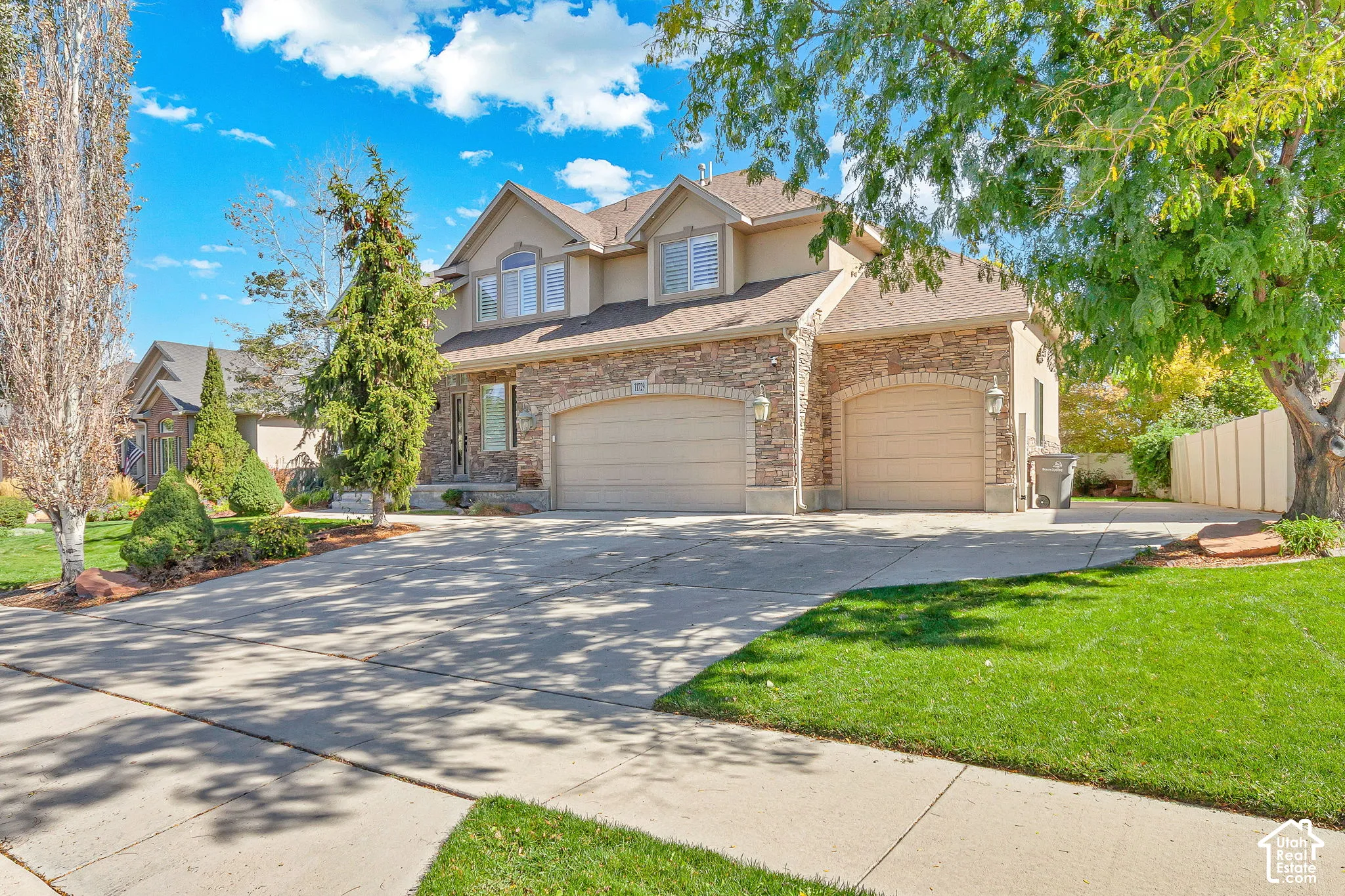 Two-story exterior featuring stone veneer siding, dual arched garage bays, dormer windows, and a concrete driveway