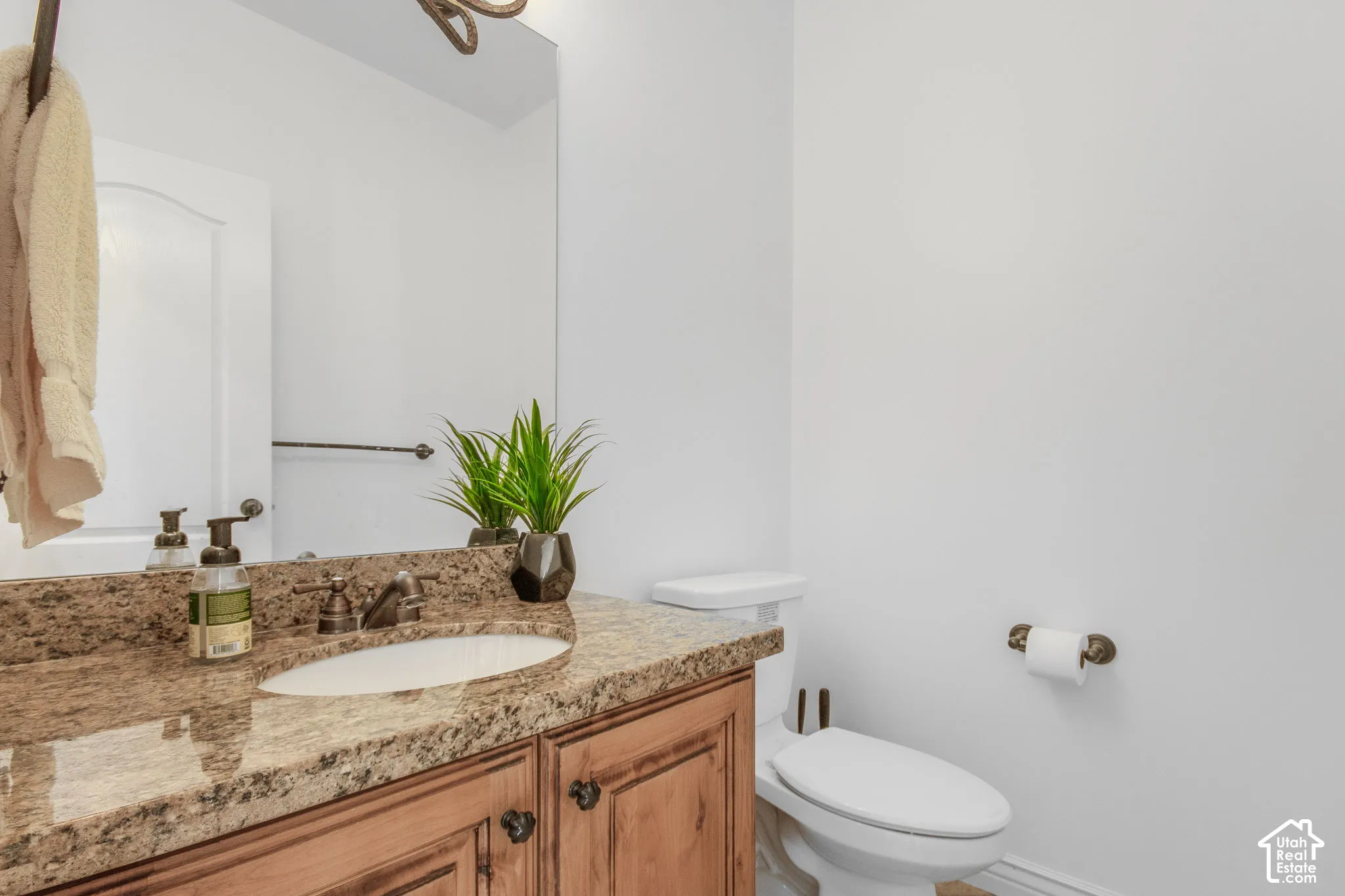Wood-finish vanity cabinet, stone-finish countertop with an integrated oval sink, large wall-mounted mirror, and oil-rubbed bronze plumbing fixtures