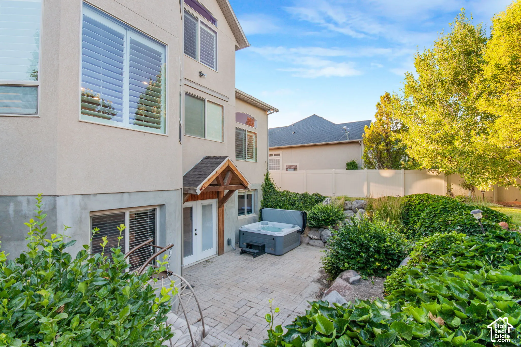 Stucco exterior with multi-level windows, paver patio, wood-frame door canopy, and integrated spa
