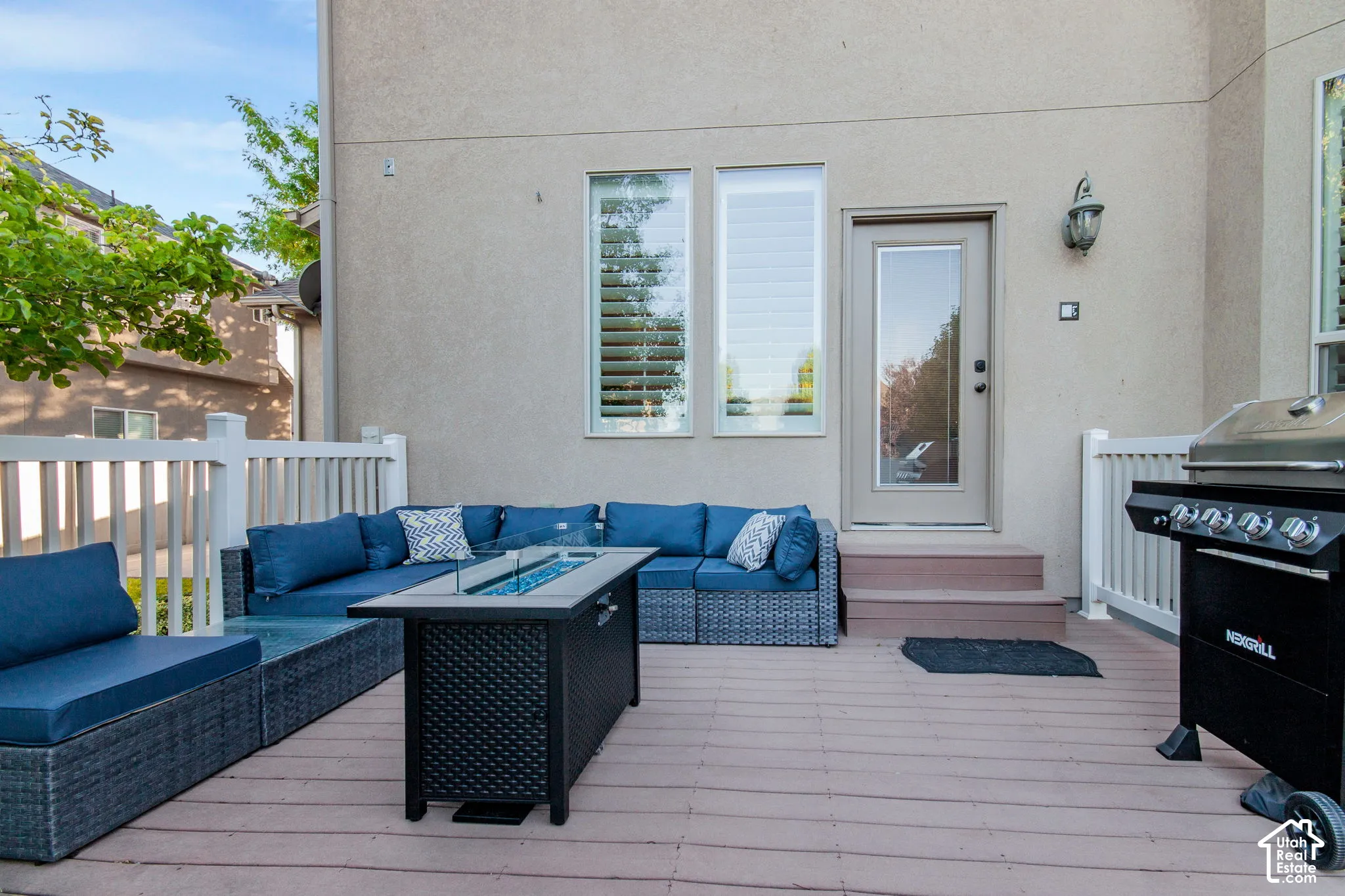 Composite deck featuring a white railing, stucco exterior wall, two vertical windows with shutters, and an exterior light fixture