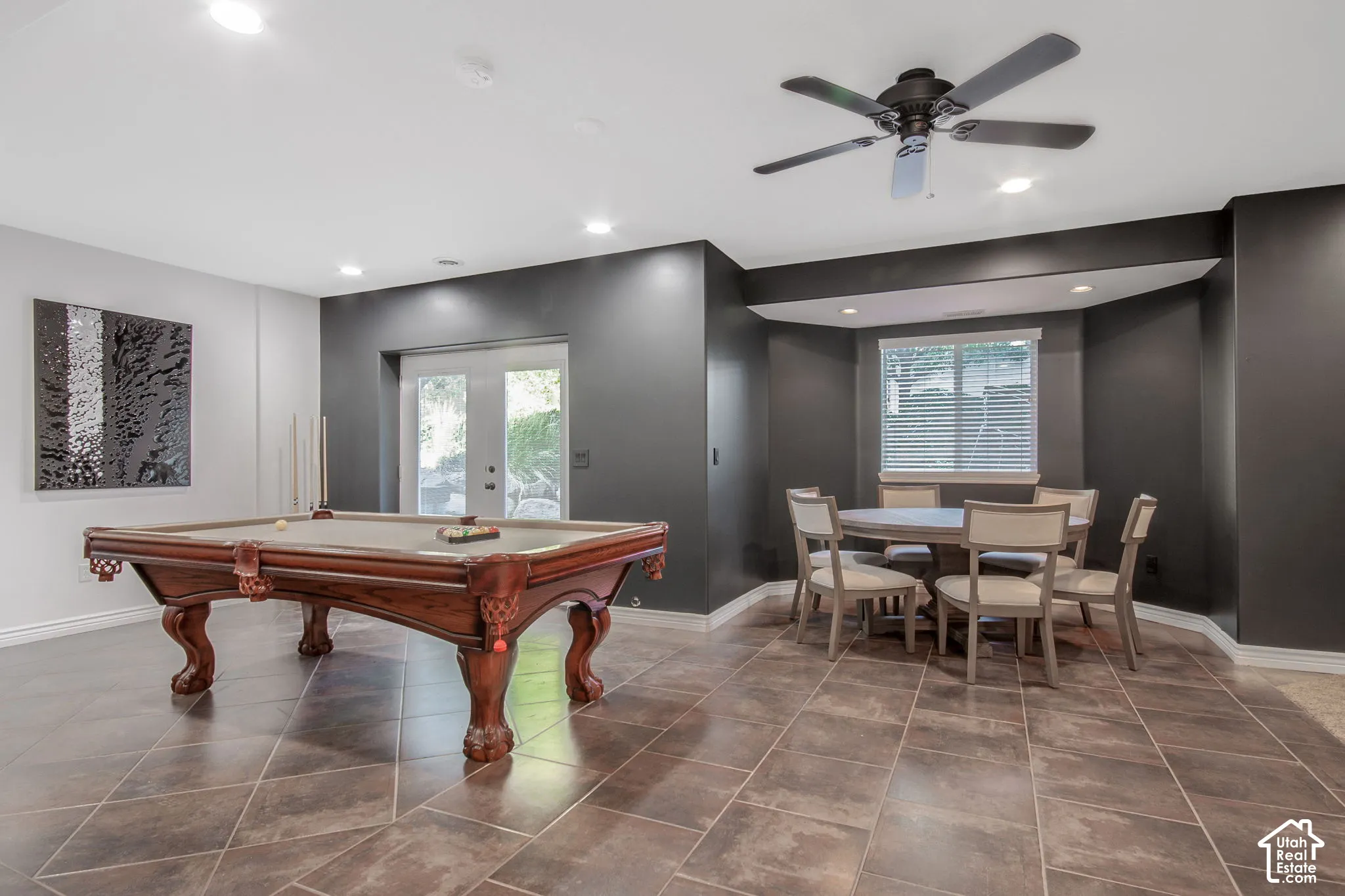 Large-format tile flooring, dual glass-panel exterior doors, recessed lighting, matte black ceiling fan, and a dedicated bay window alcove