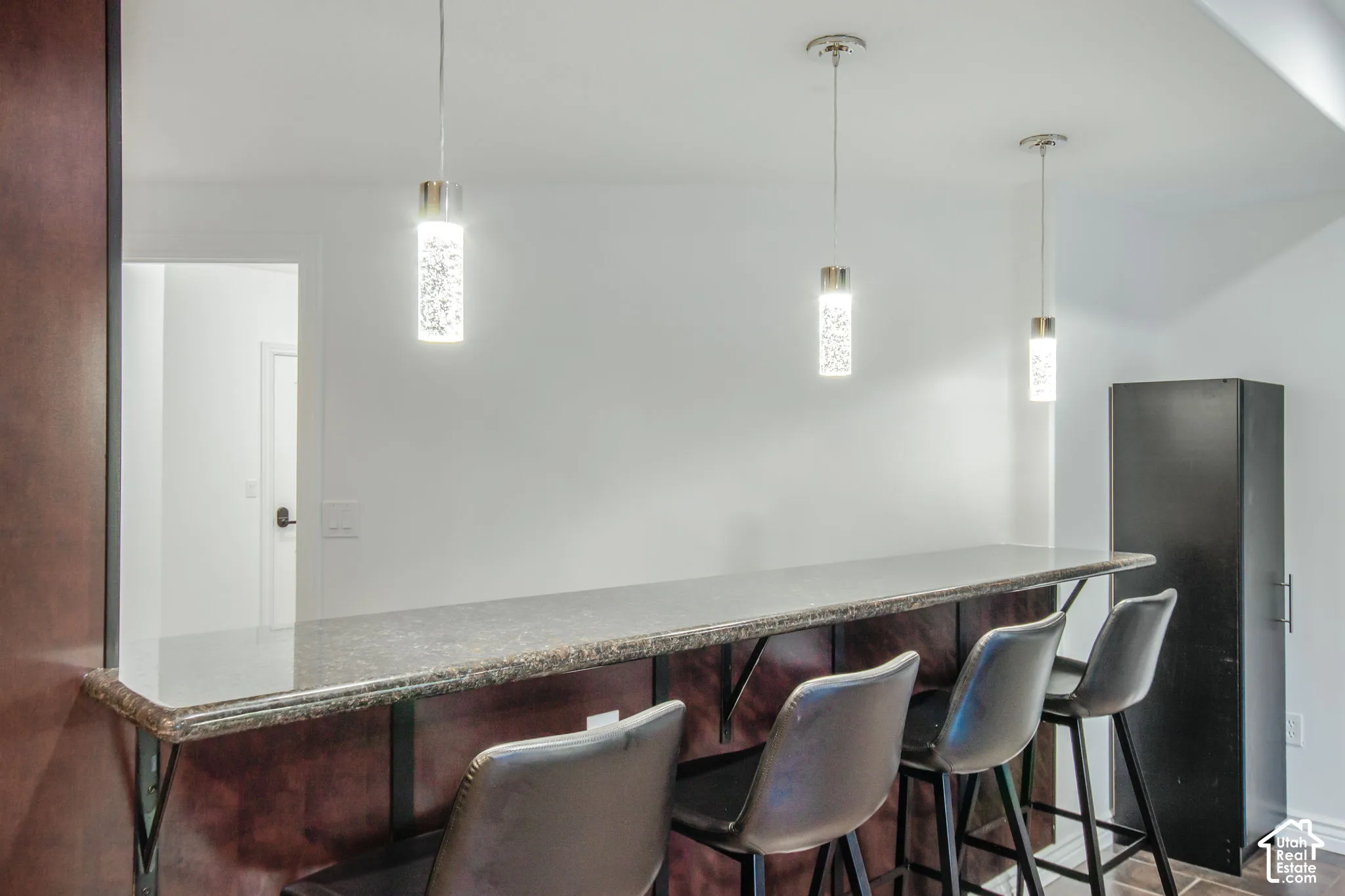 Breakfast bar featuring a stone-composite countertop, dark wood-finish cabinetry, and three modern cylindrical pendant lights