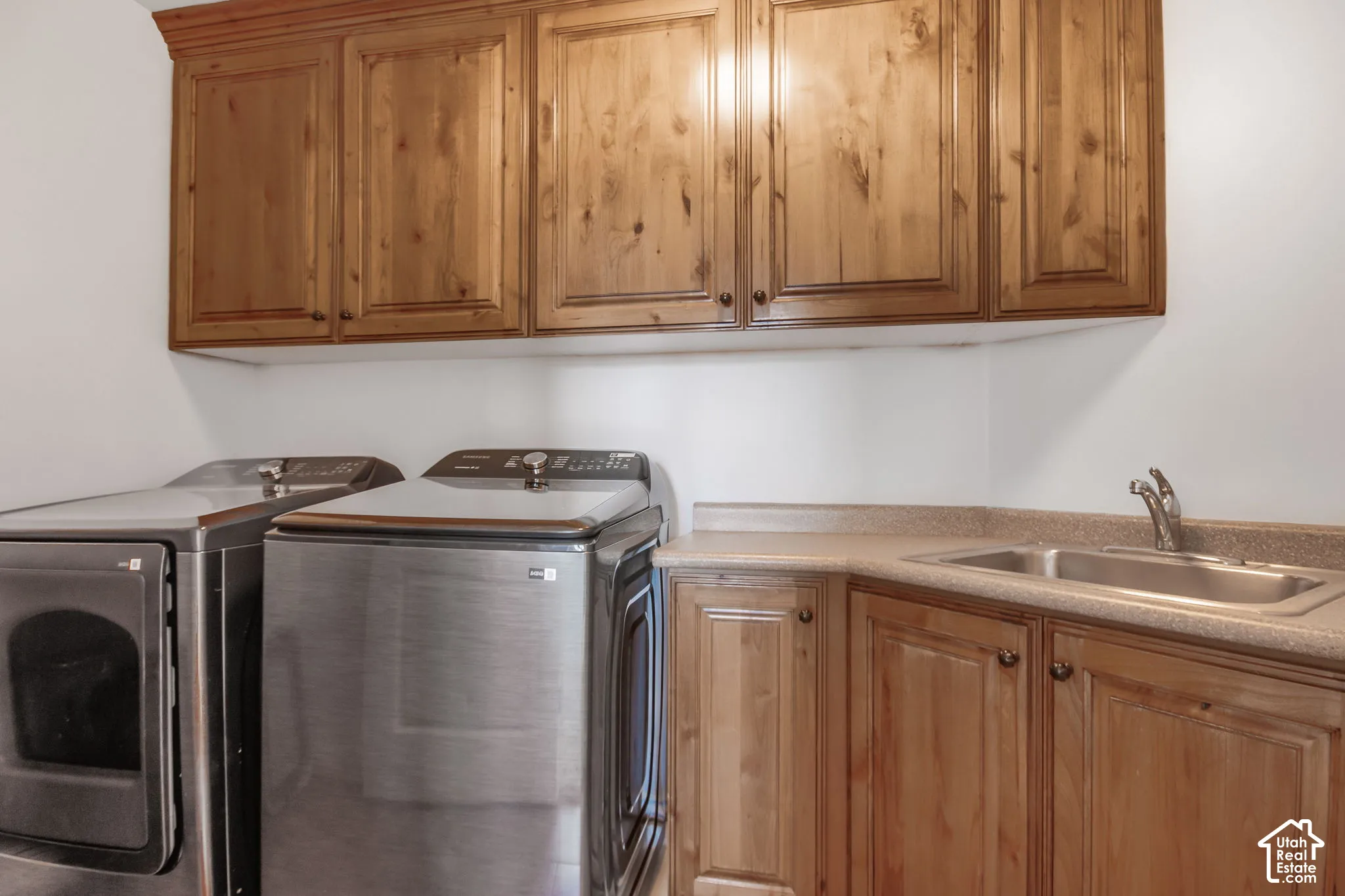 Utility space featuring stained wood cabinetry, solid surface countertop with an integrated drop-in sink, and chrome faucet hardware