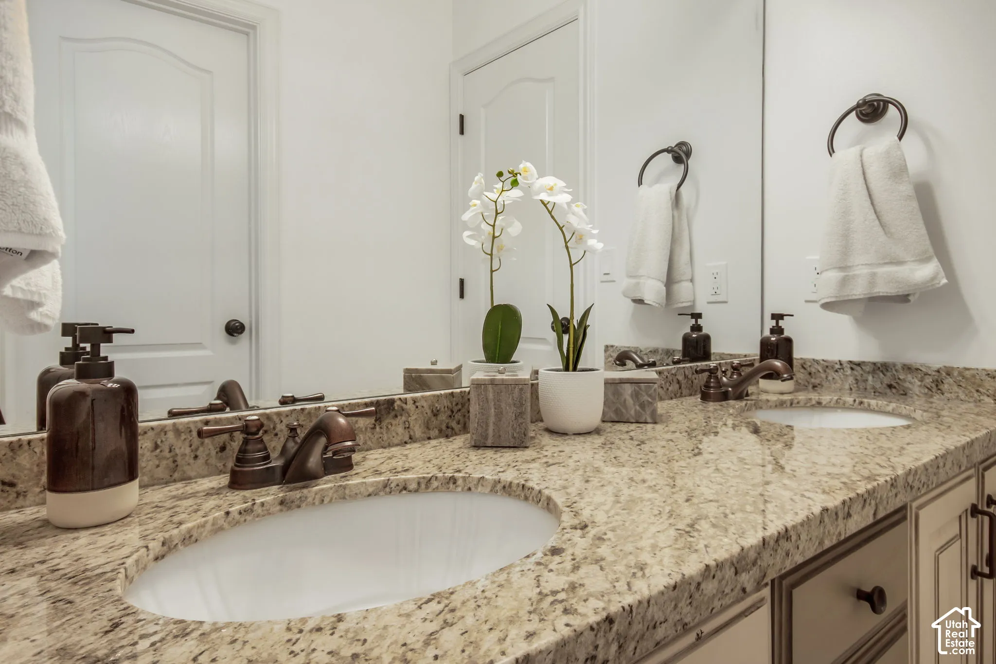 Dual-sink vanity featuring stone-composite countertop, undermount oval basins, oil-rubbed bronze faucets, and cabinetry hardware