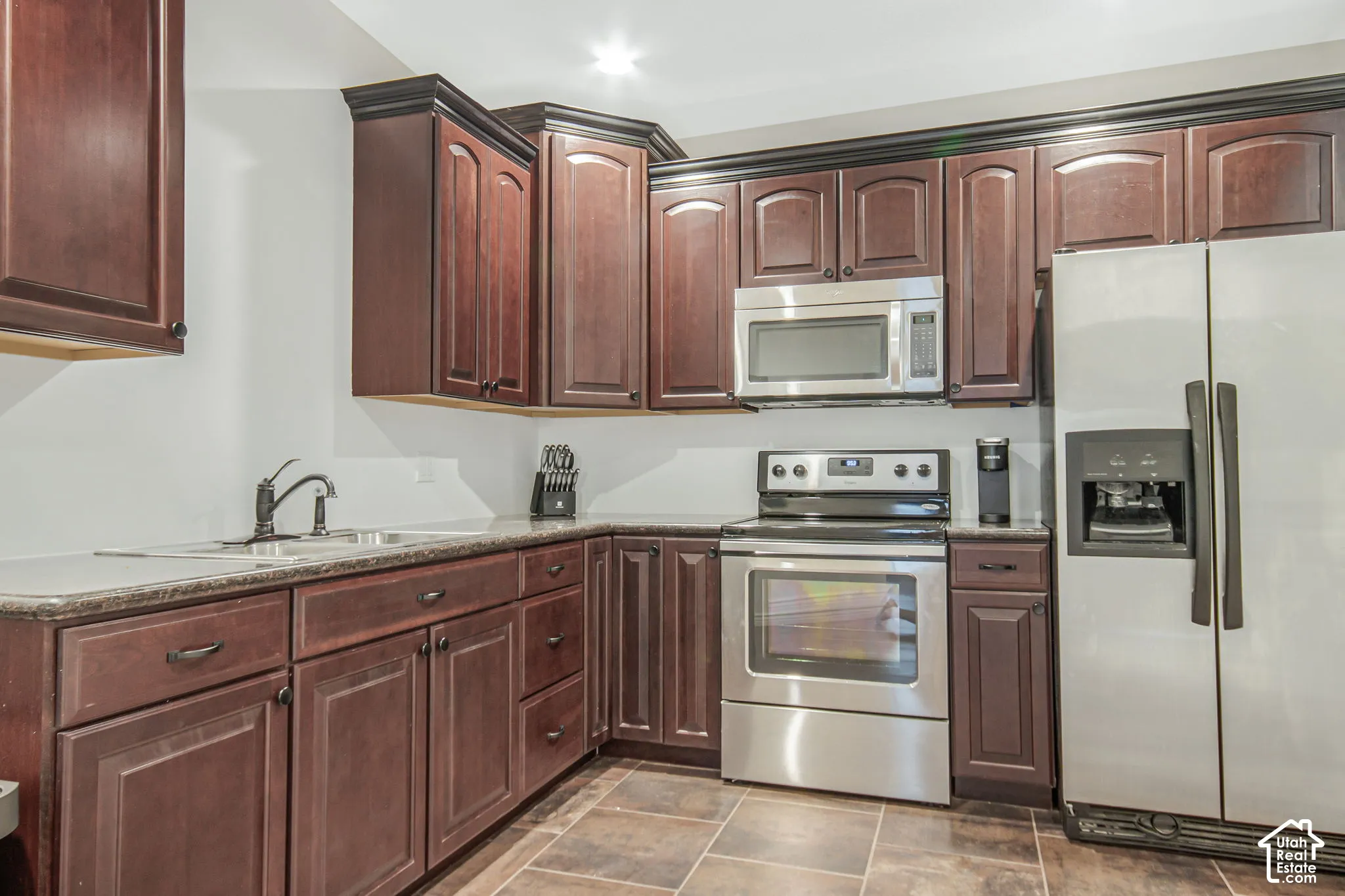 Kitchen featuring dark-toned wooden cabinetry, stone-finish countertops, stainless steel appliances, and tile flooring