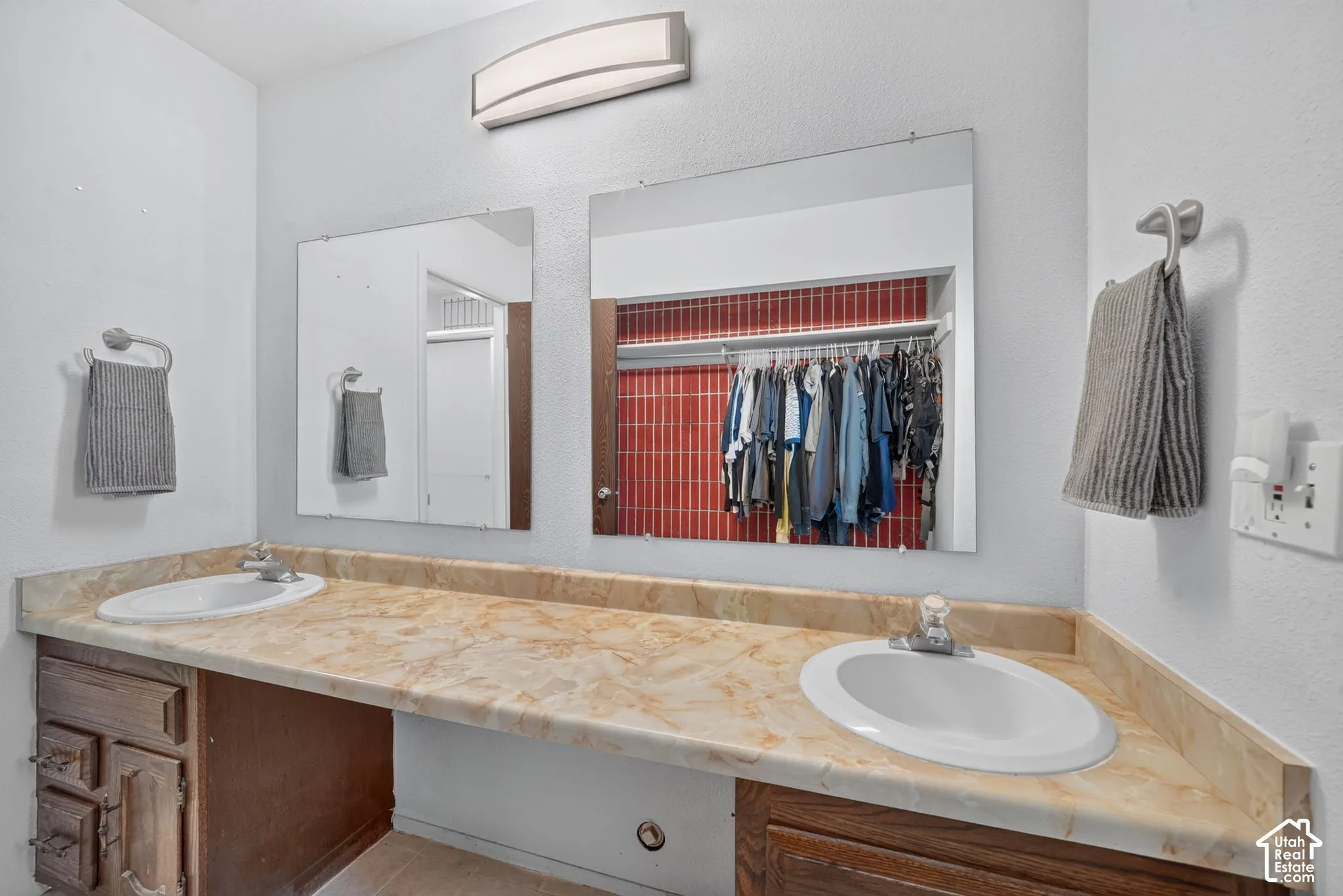 Primary Bathroom. Dual-sink vanity featuring a stone-patterned countertop, wooden cabinetry, two integrated mirrors, and a wall-mounted light fixture