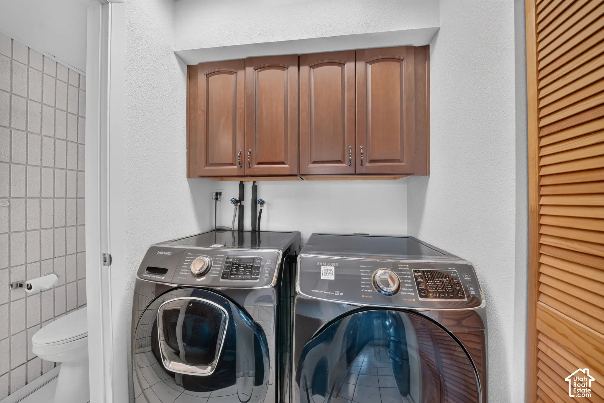 Laundry area featuring dark wood-finish cabinetry, tile flooring, and louvered doors