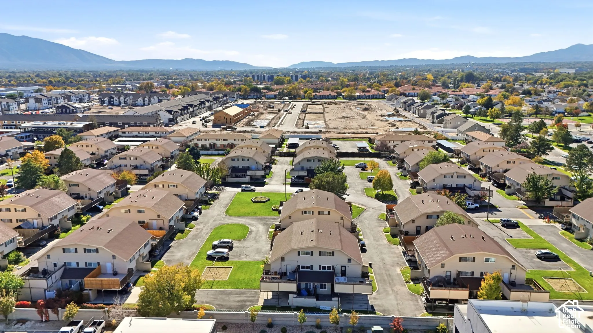 Aerial perspective of a multi-unit residential community featuring brown shingle roofing, asphalt paving, maintained green spaces, and a mountain backdrop