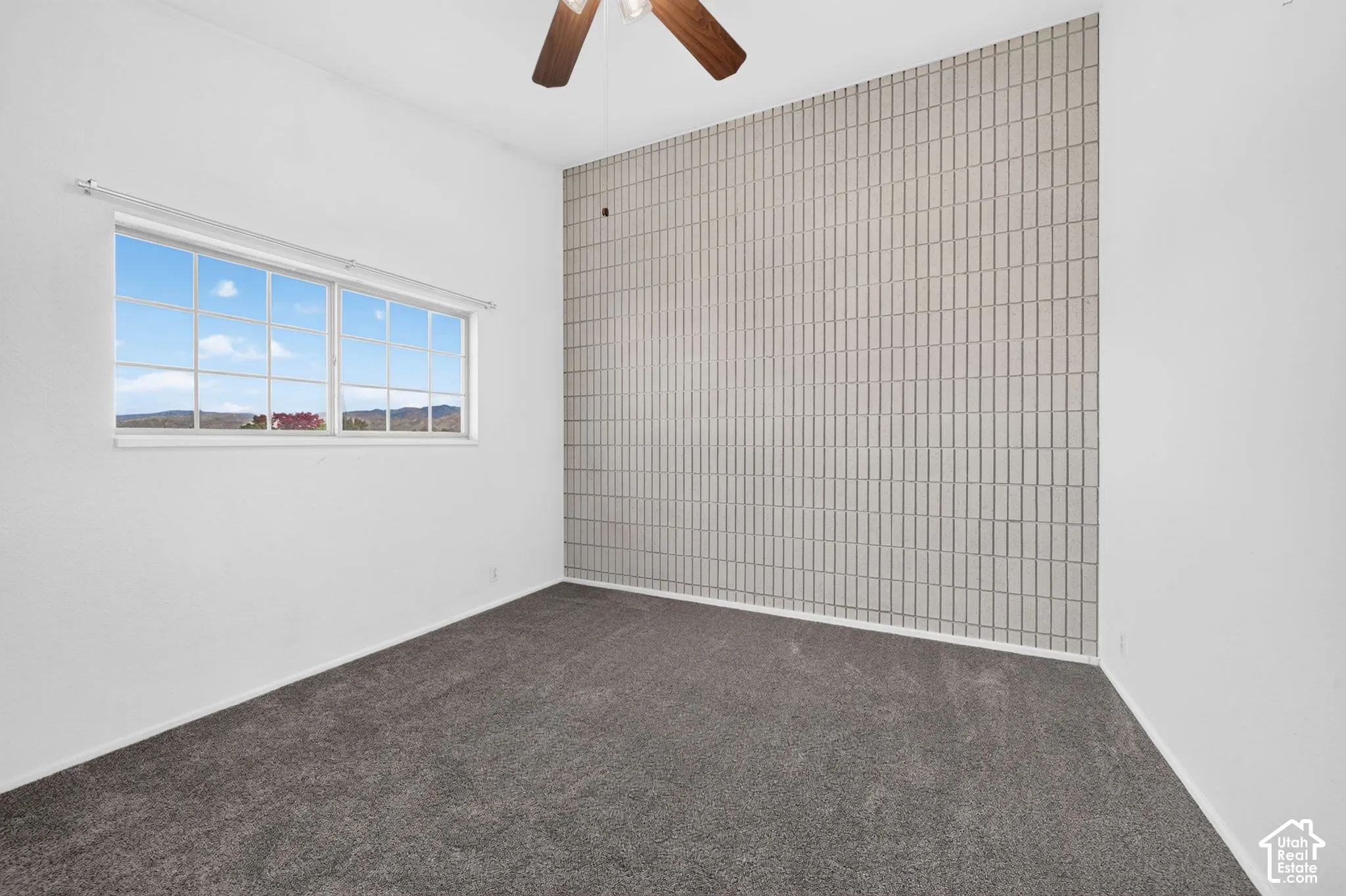 Room featuring a floor-to-ceiling textured tile accent wall, wall-to-wall carpeting, and a multi-pane window with mountain scenery