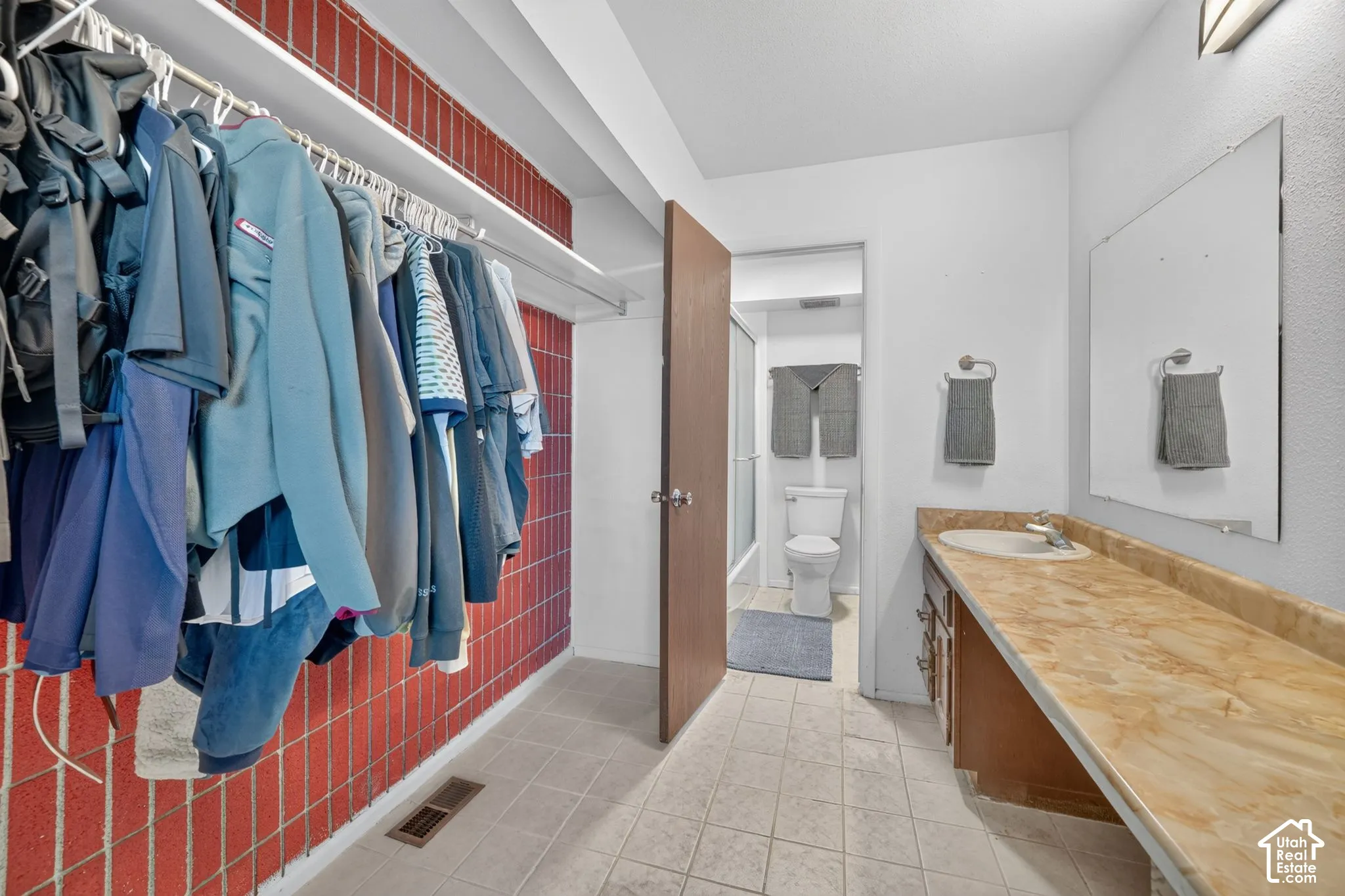Primary Walk through closet & dressing area featuring built-in clothing rod, Primary bathroom solid-surface vanity countertop, integrated sink, large wall-mounted mirror, and ceramic tile flooring