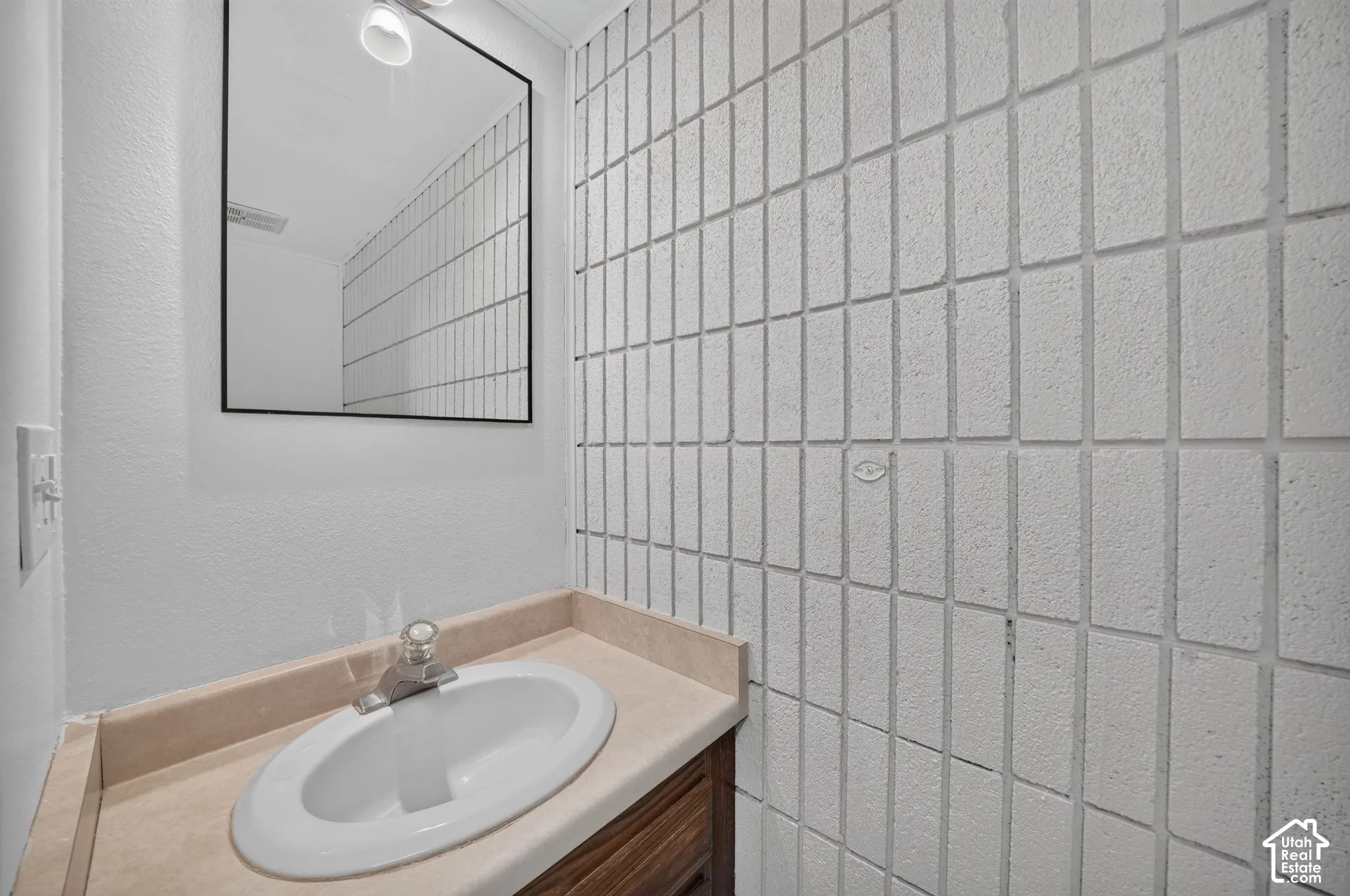 Half Bath off the kitchen. New toilet. Wall-mounted rectangular mirror with a black frame, textured white vertical tile accent wall, vanity with a solid-surface integrated countertop, and a recessed oval basin