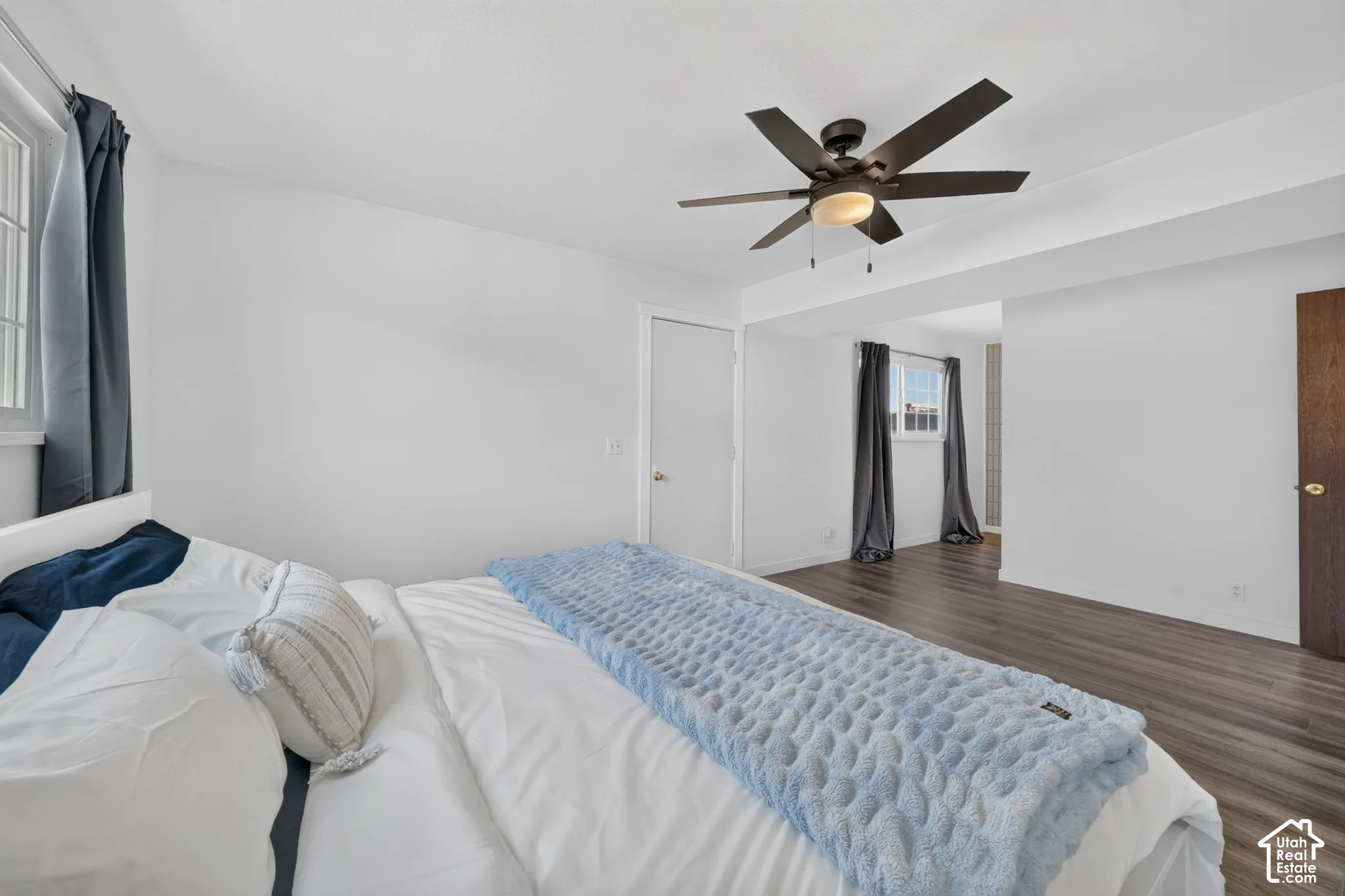 Room featuring wood-finish flooring, a multi-blade ceiling fan with integrated lighting, and multiple windows