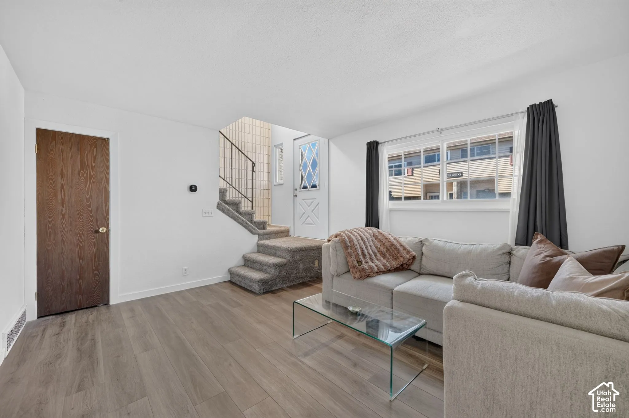 Living area featuring wood-finish flooring, multi-pane window, staircase with metal railing, and solid-core interior door