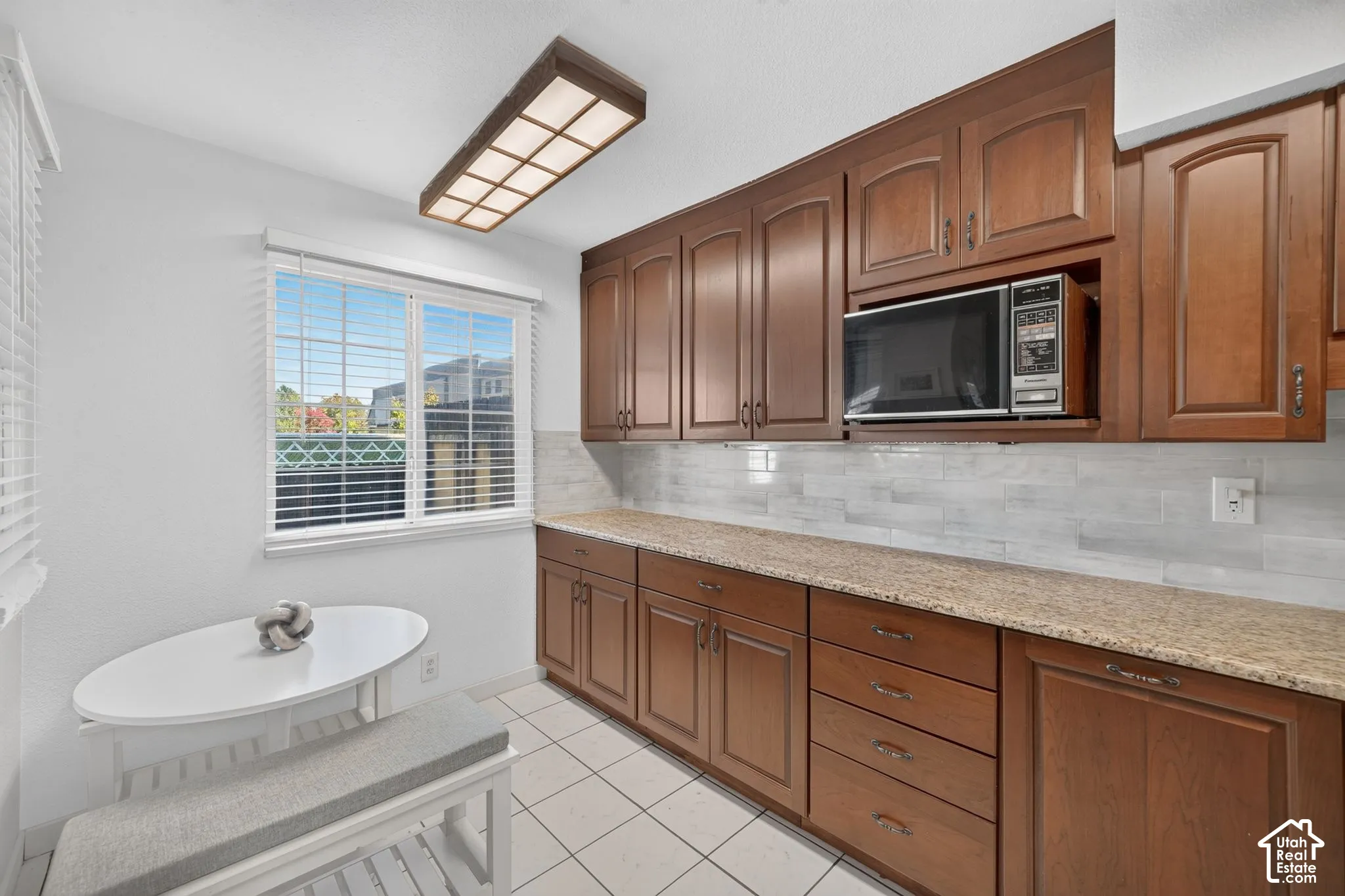 Kitchen area featuring medium-tone wood cabinetry, stone-patterned countertops, a subway-tile backsplash, tile flooring, and a built-in microwave