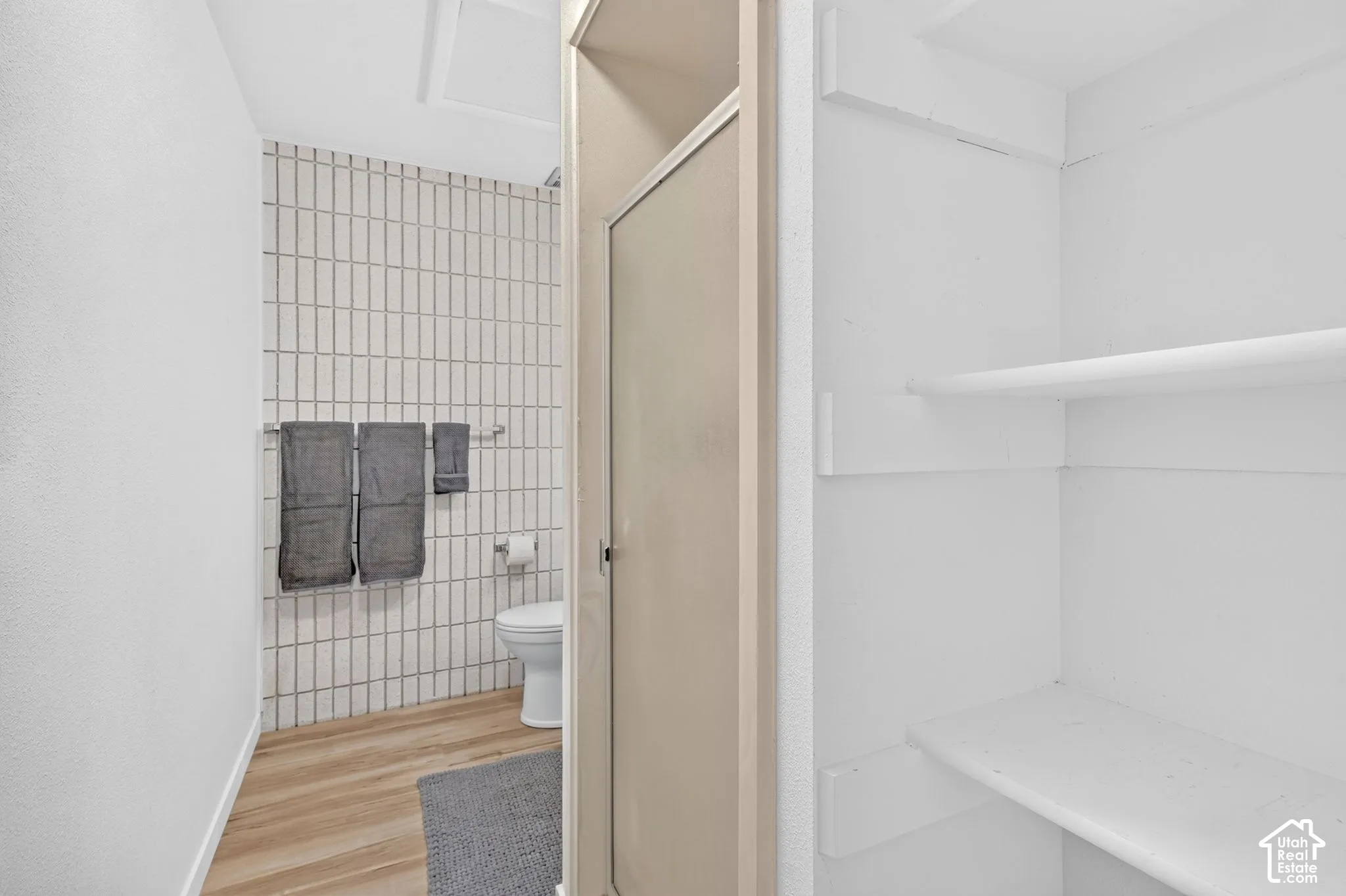 Bathroom featuring floor-to-ceiling vertical tile wall surfacing, wood-finish flooring, a wall-mounted toilet, and built-in shelving