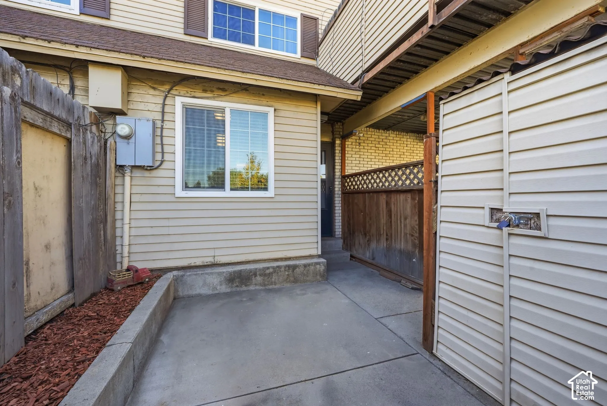 Exterior patio area featuring concrete hardscaping, horizontal vinyl siding, enclosed wood fencing with lattice detailing, and an integrated exterior storage unit