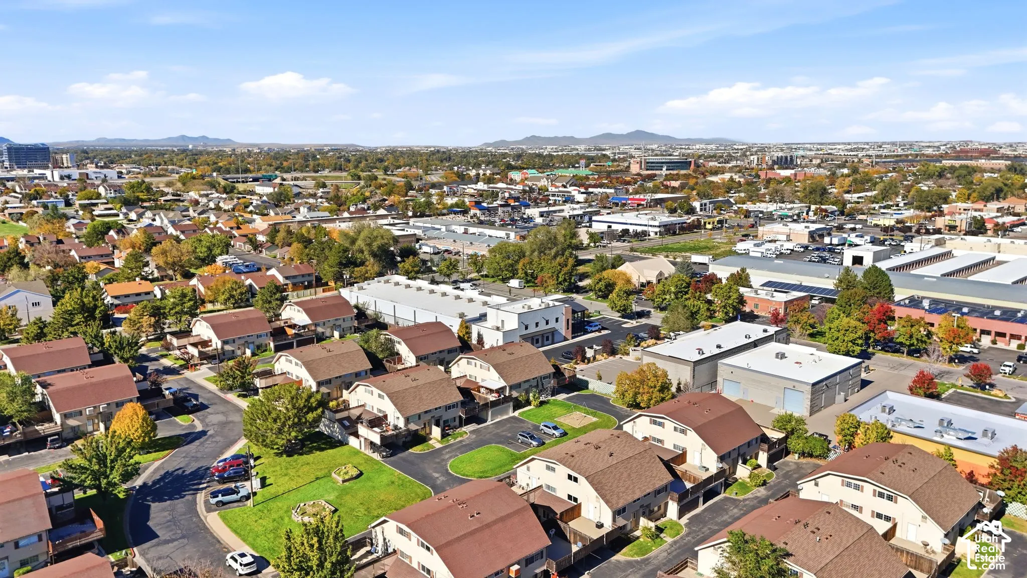 Aerial perspective of a multi-family residential complex featuring asphalt shingle roofing, paved common driveways, curated lawn spaces, and a mountainous horizon