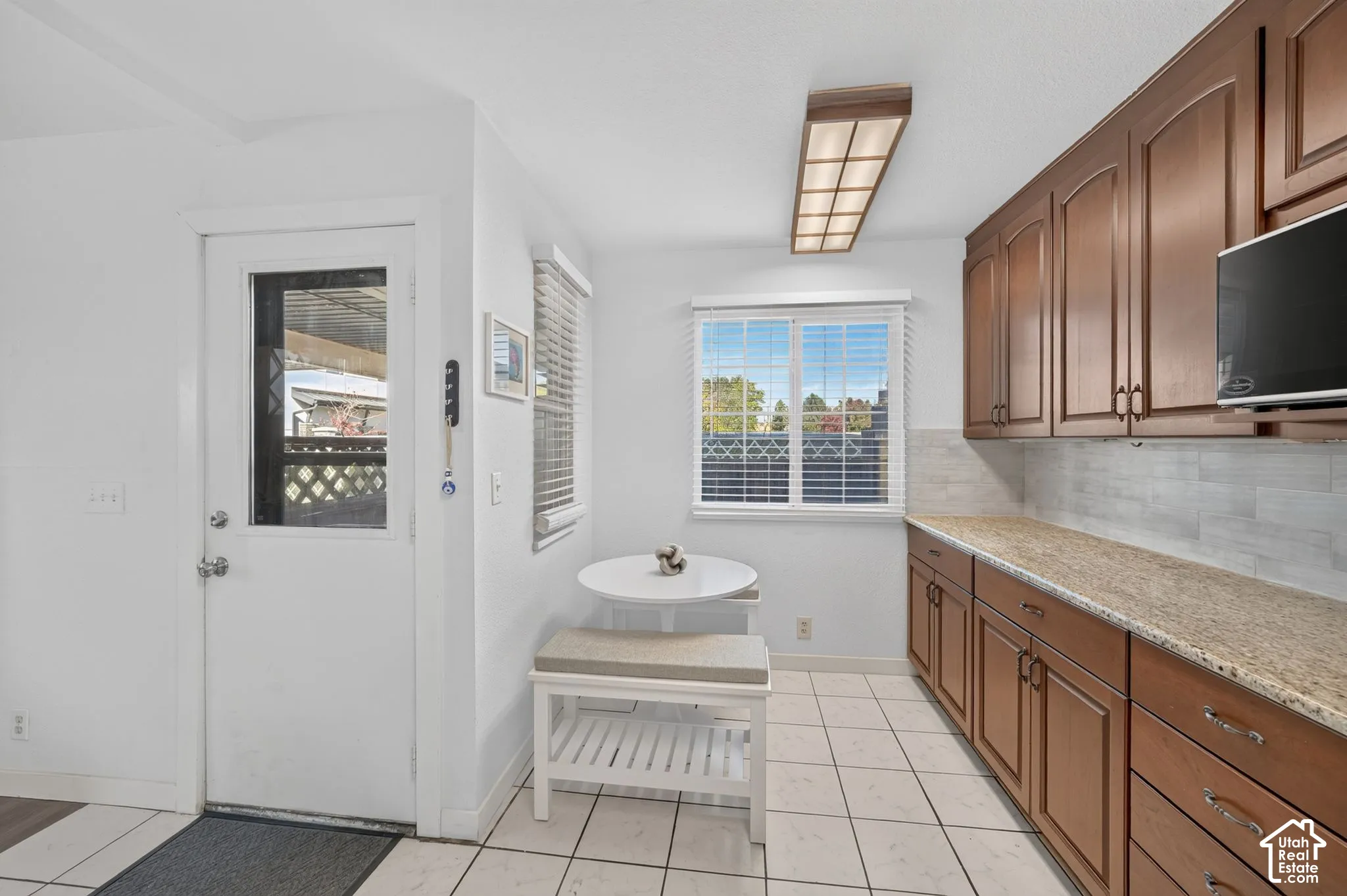 Kitchen area featuring wood cabinetry, stone countertops, tiled backsplash, ceramic tile flooring, and flush-mount ceiling lighting