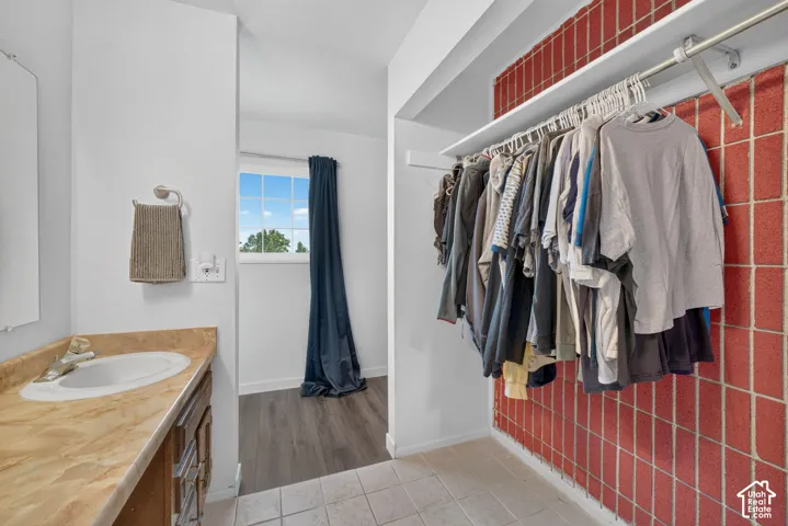 Vanity with a solid-surface countertop and integrated sink, complemented by ceramic tile flooring and a built-in clothing rod featuring overhead shelving against a grid-textured wall