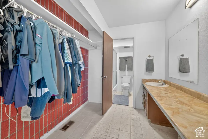 Primary Walk through closet & dressing area featuring built-in clothing rod, Primary bathroom solid-surface vanity countertop, integrated sink, large wall-mounted mirror, and ceramic tile flooring