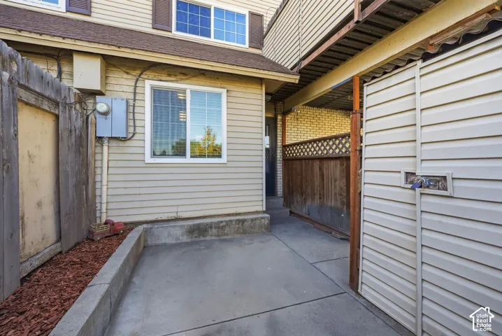 Exterior patio area featuring concrete hardscaping, horizontal vinyl siding, enclosed wood fencing with lattice detailing, and an integrated exterior storage unit