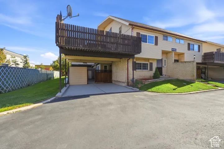 Multi-level exterior featuring a covered carport, elevated wood-slat balcony, brick and siding facade, and fenced outdoor space