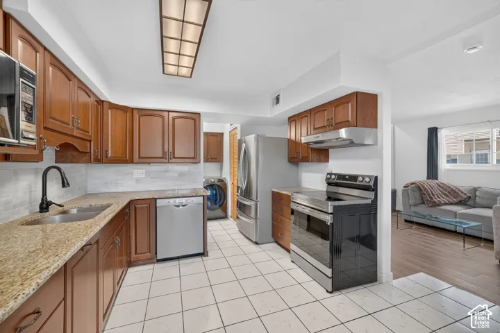 Kitchen featuring wood cabinetry, stone-finish countertops, tile flooring, stainless steel appliances, and a tile backsplash