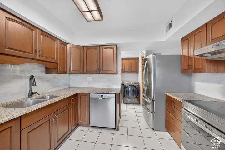 Kitchen featuring stained wood cabinetry, stone countertops, tiled backsplash, stainless steel appliances, and tile flooring