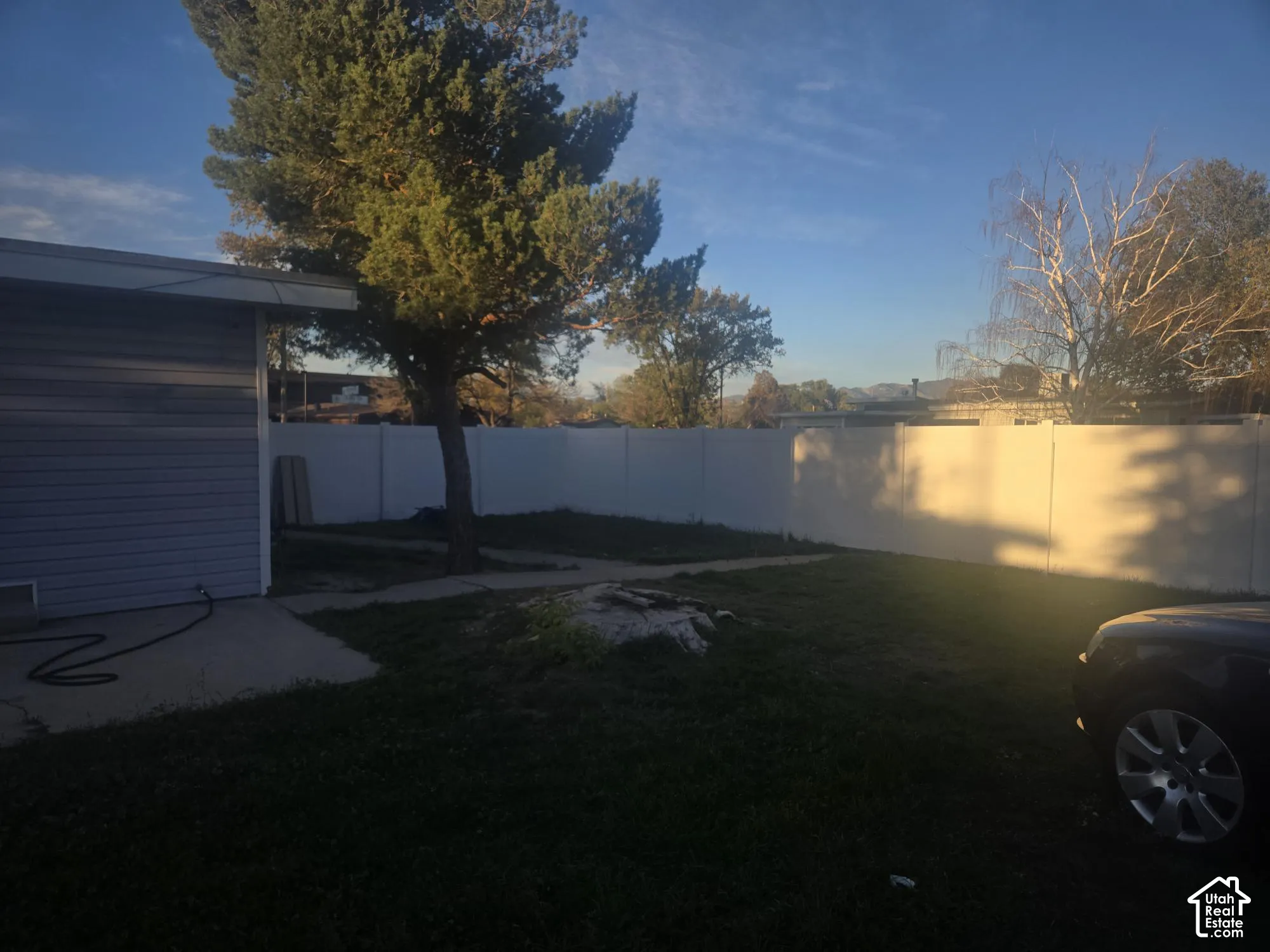 Rear exterior featuring a concrete patio, white vinyl privacy fencing, and mature trees