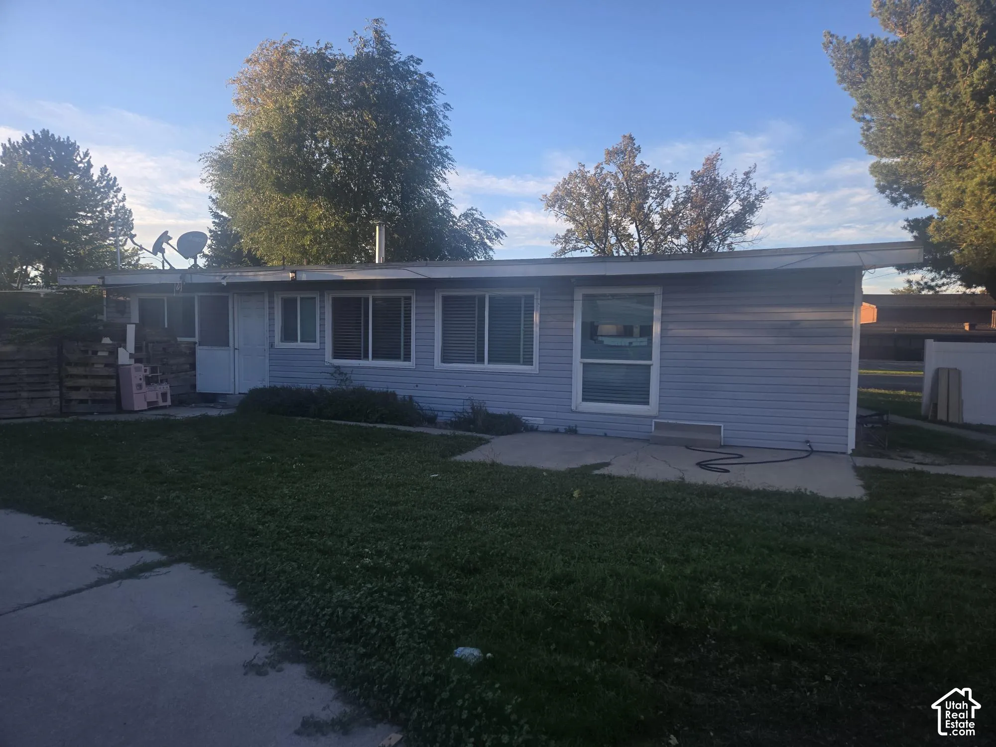 Single-story exterior featuring light blue horizontal siding, a flat roofline, sliding glass door, and an attached concrete patio