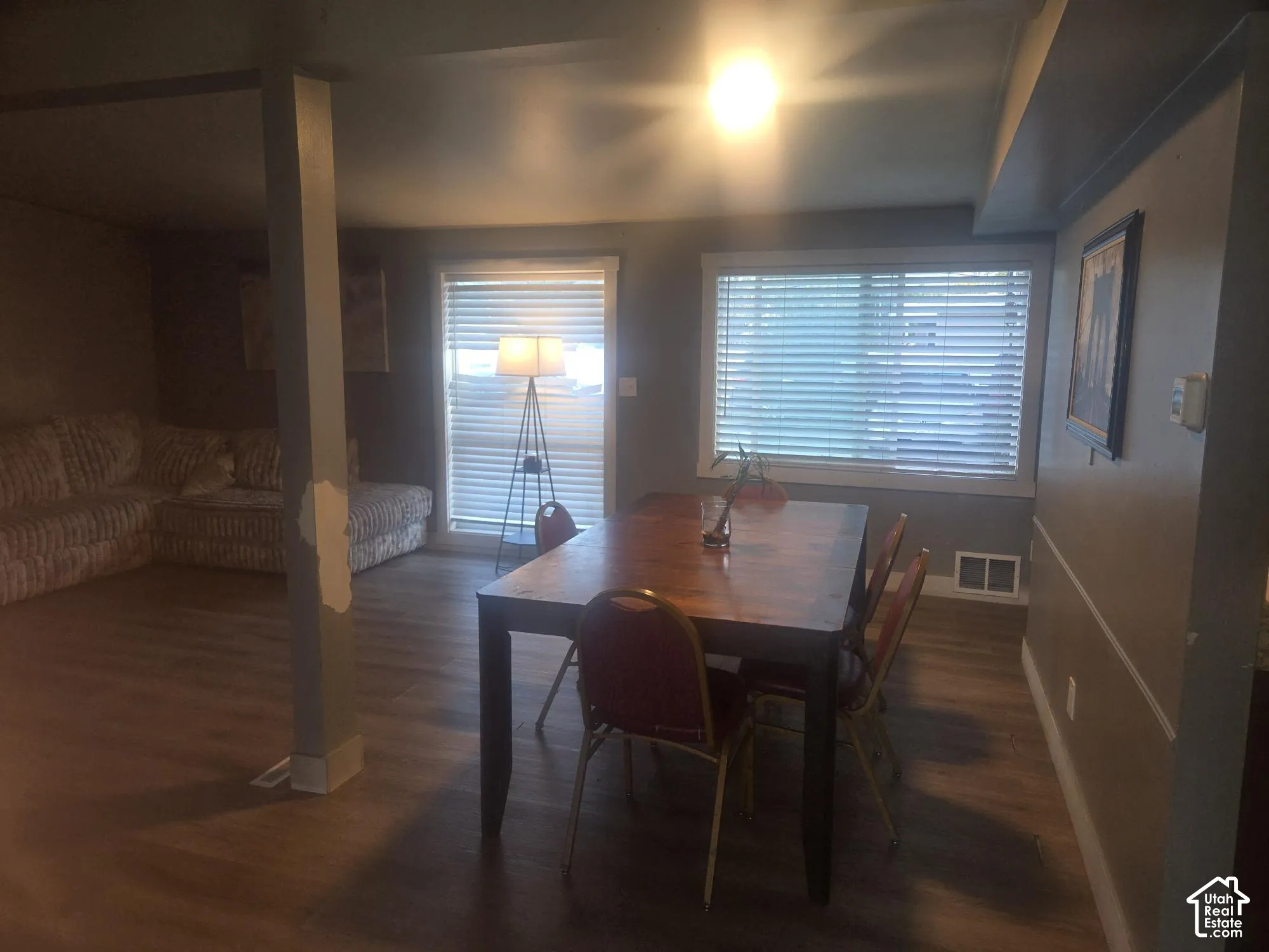 Open-concept area featuring wood-finish flooring, two sets of windows with horizontal blinds, and a neutral wall palette