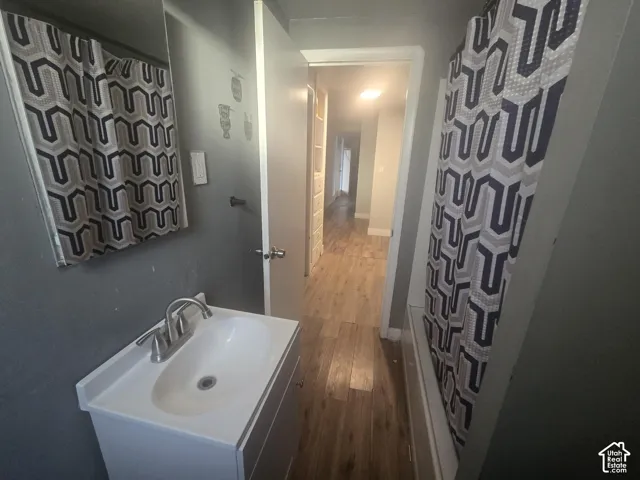 Bathroom featuring a vanity with an integrated basin, a polished chrome high-arc faucet, a wall-mounted mirror, and wood-finish flooring