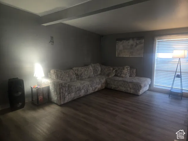 Living area featuring wood-finish flooring, a recessed ceiling beam, and horizontal slat window blinds