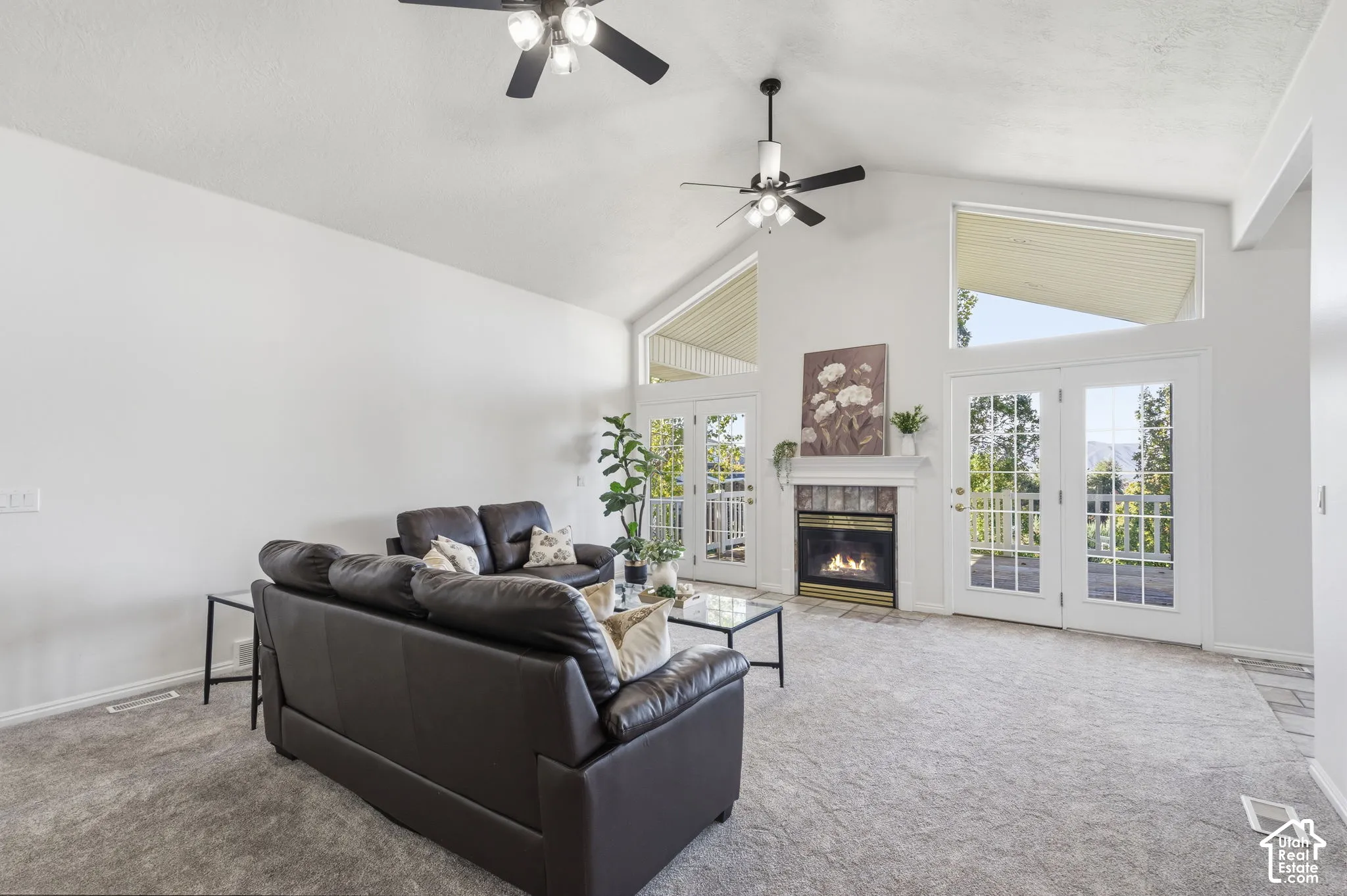 Vaulted ceiling featuring dual ceiling fans, gas fireplace with tile surround, and expansive glass-paneled double doors with transom windows