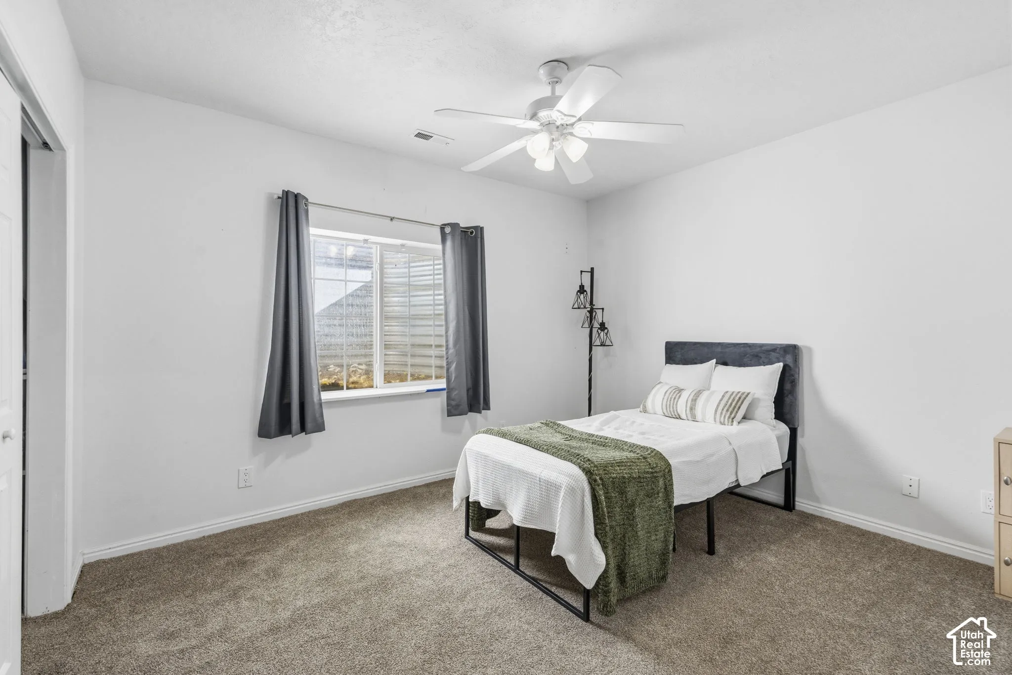 Neutral-toned carpeted flooring, white wall finish, slider window, and ceiling-mounted light fixture with integrated fan