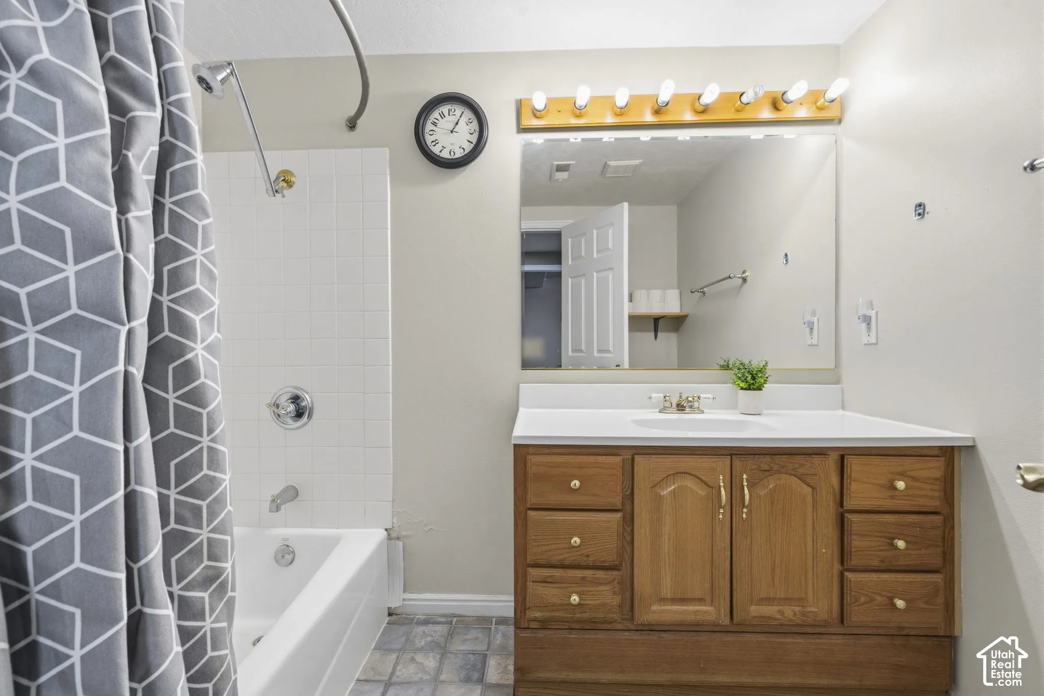Bathroom featuring a wood-finish vanity with built-in storage drawers, a large wall-mounted mirror, a multi-bulb light fixture, and a white tiled tub surround