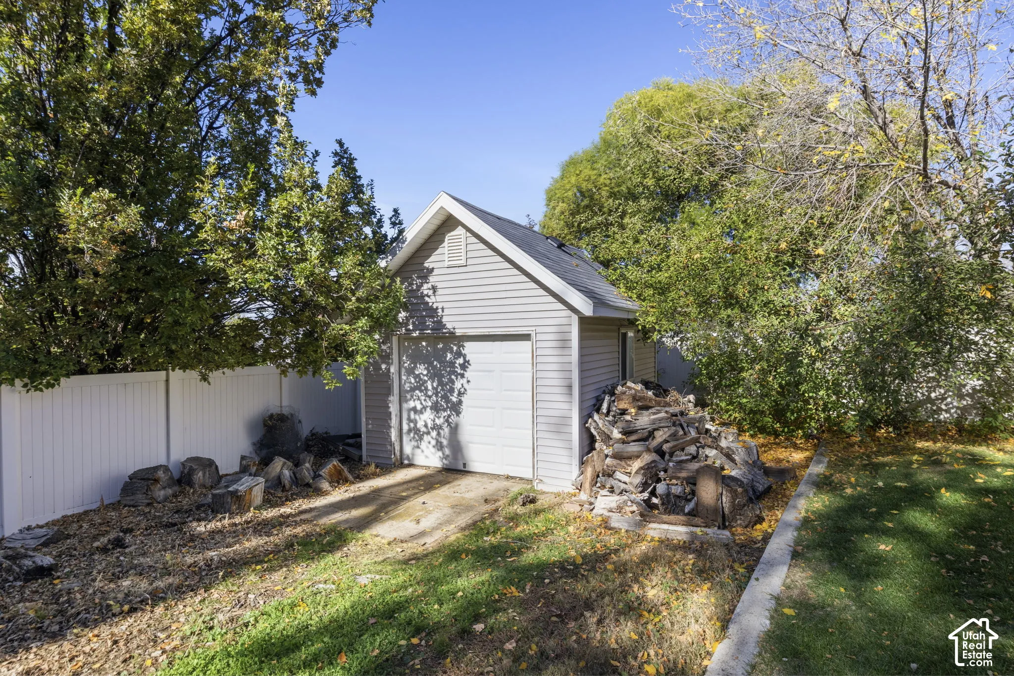 Detached garage with light-colored siding, a gabled roofline, and a solid-panel overhead door, situated within a fenced perimeter