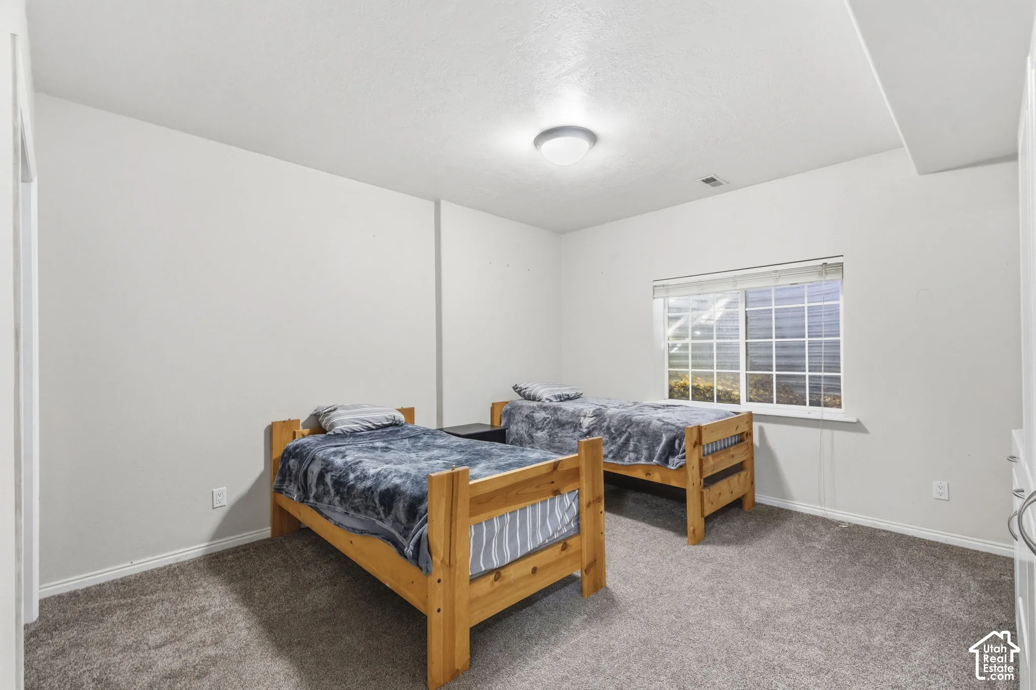 Room featuring neutral wall tones, gray carpeting, a single ceiling-mounted flush light fixture, and a large sliding window with blinds