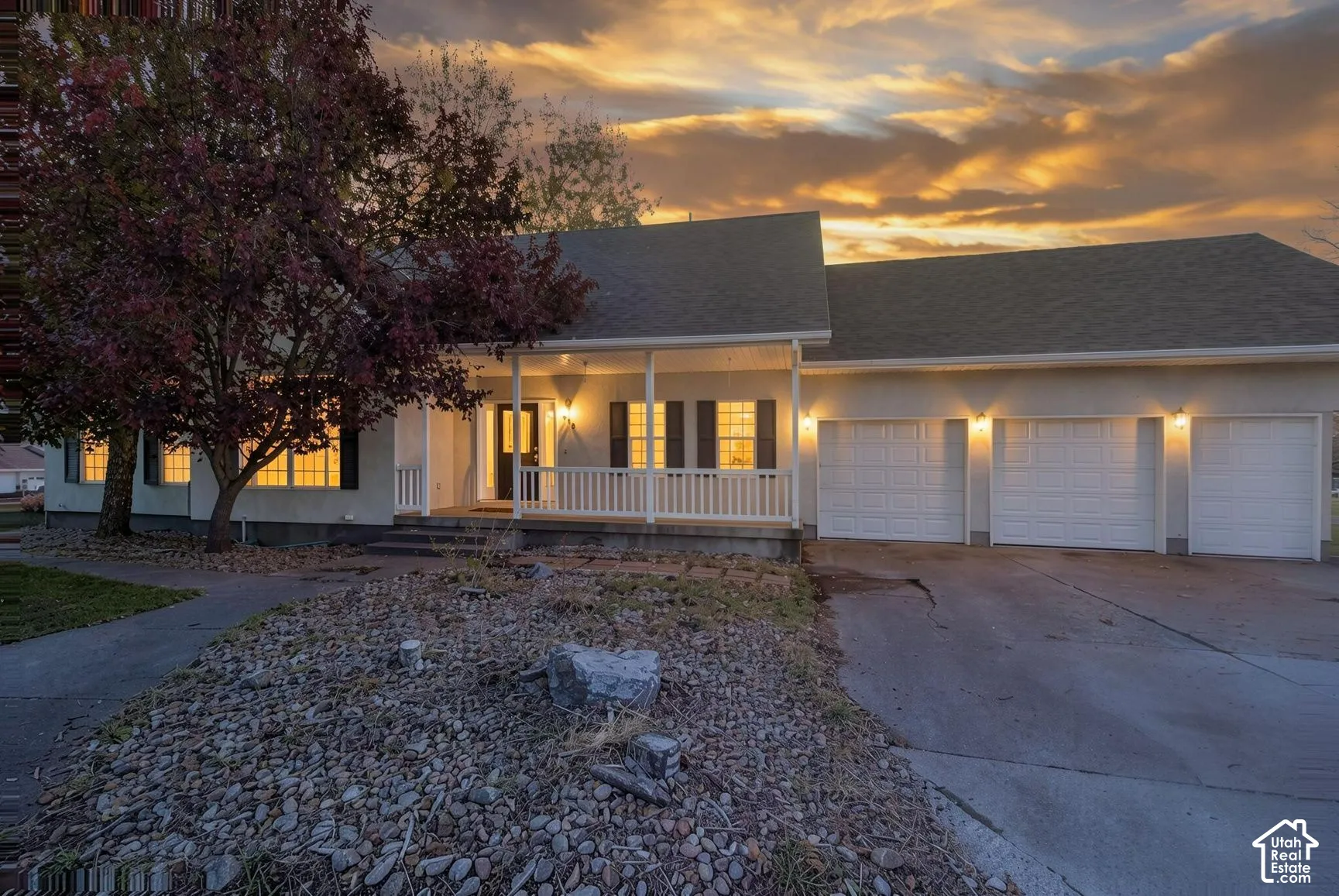 Single-story exterior featuring a covered front porch with white railing, three-car garage, multi-pane windows, and concrete driveway