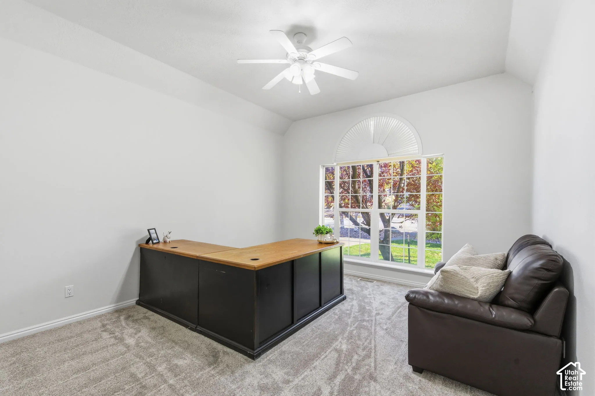Neutral-toned room featuring a vaulted ceiling, ceiling fan with integrated light fixture, and a large window with an arched transom