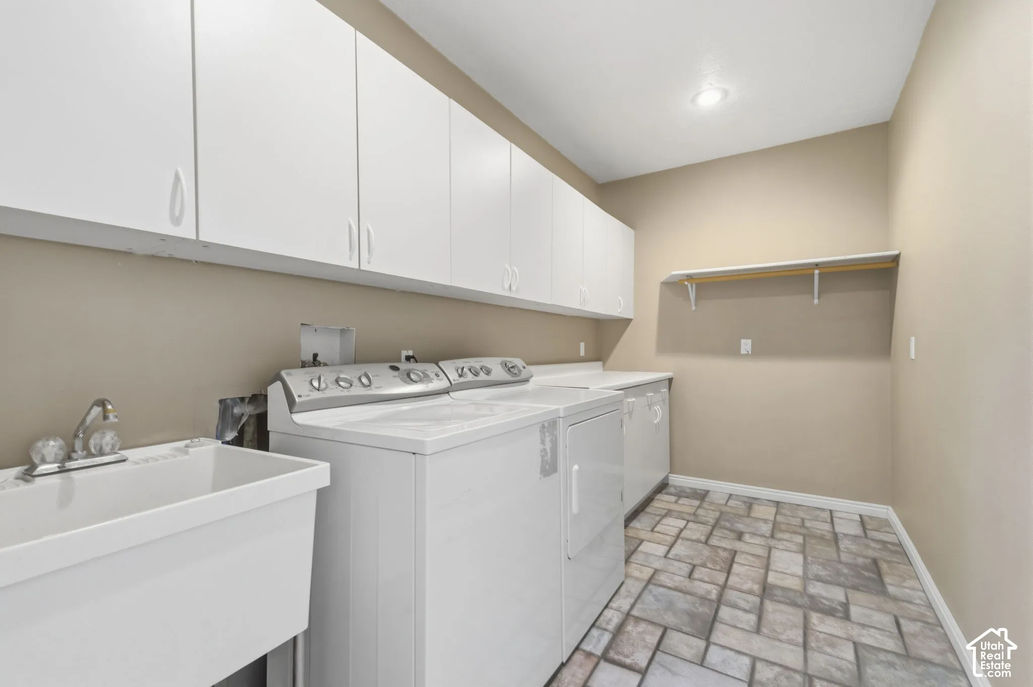 Laundry area featuring full-wall white cabinetry, utility sink, stone-finish tile flooring, and integrated wall shelving