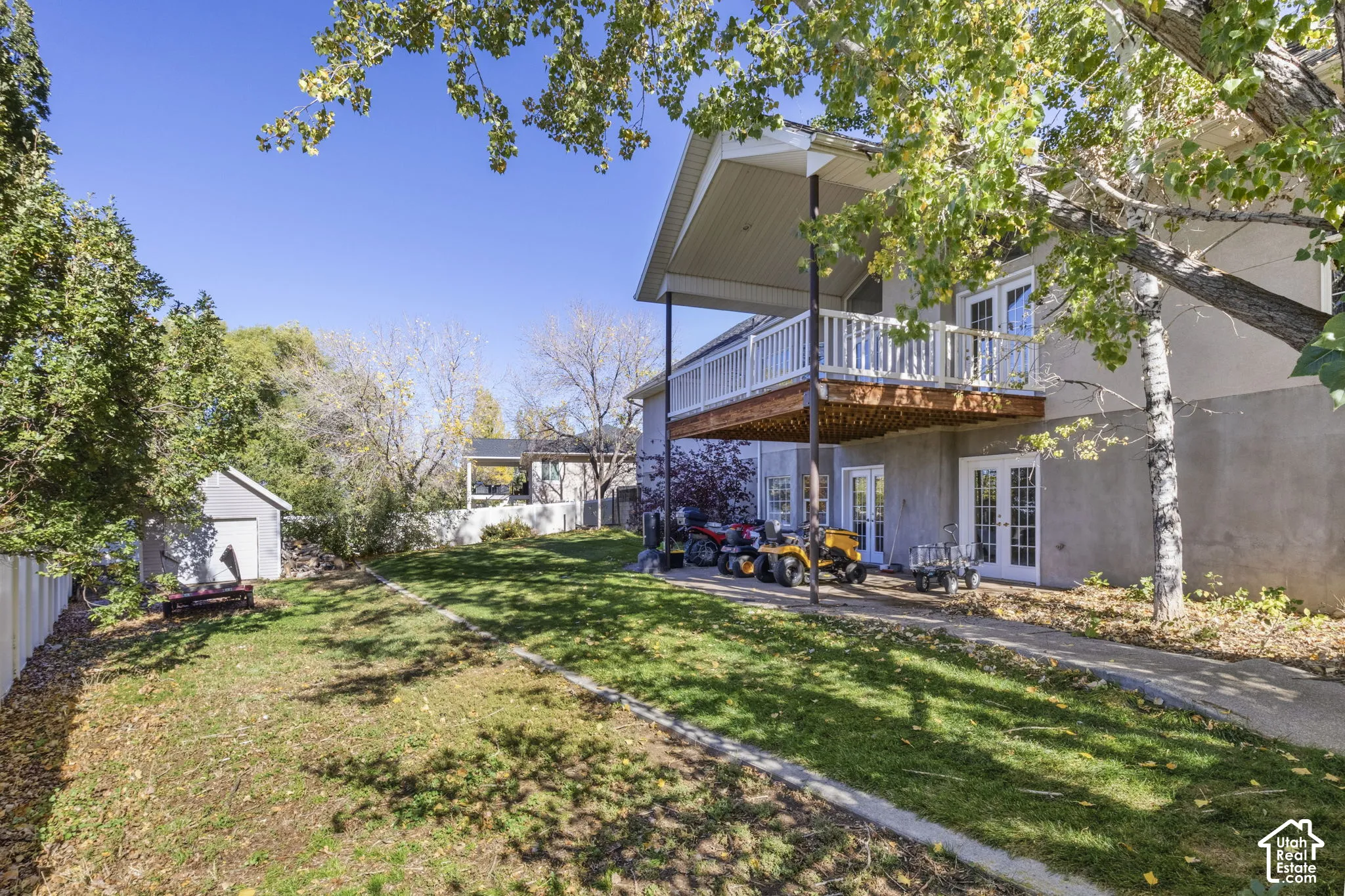 Expansive backyard featuring a manicured lawn, elevated wood deck with white railings, concrete patio, and a detached storage shed enclosed by perimeter fencing