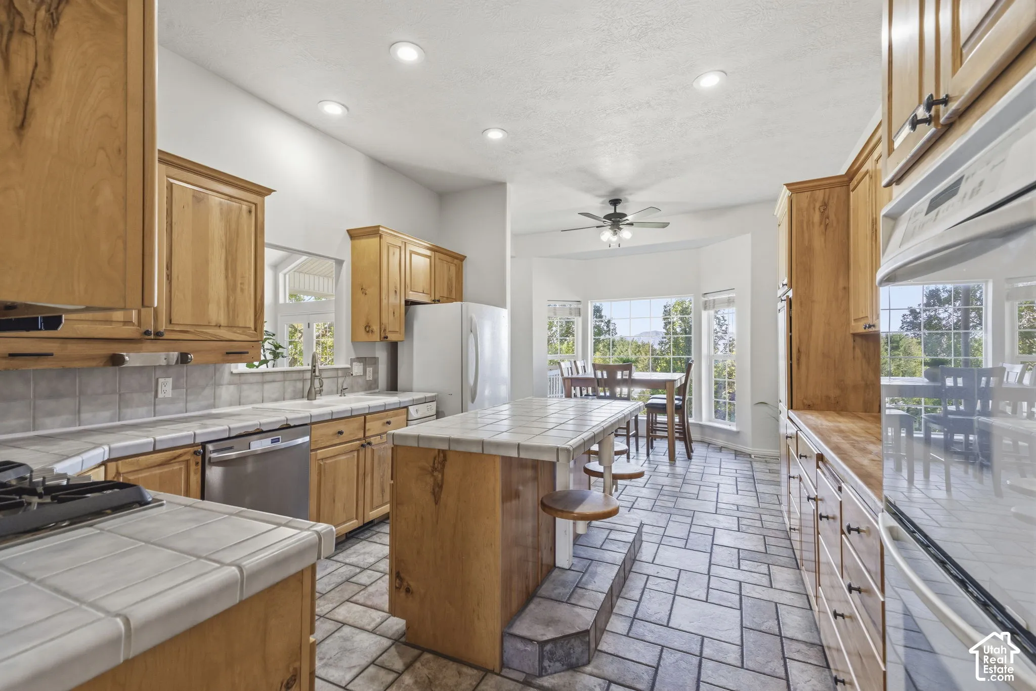 Kitchen featuring wood cabinetry, tile countertops, a central island with bar seating, tiled flooring, and recessed lighting