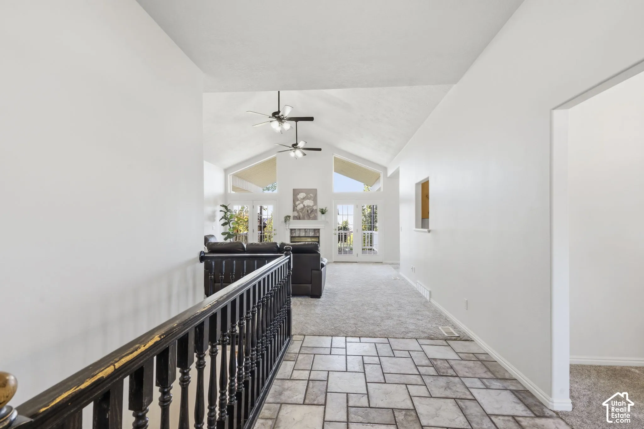 Vaulted ceiling with dual ceiling fans, tile flooring, stone-faced fireplace, and expansive windows