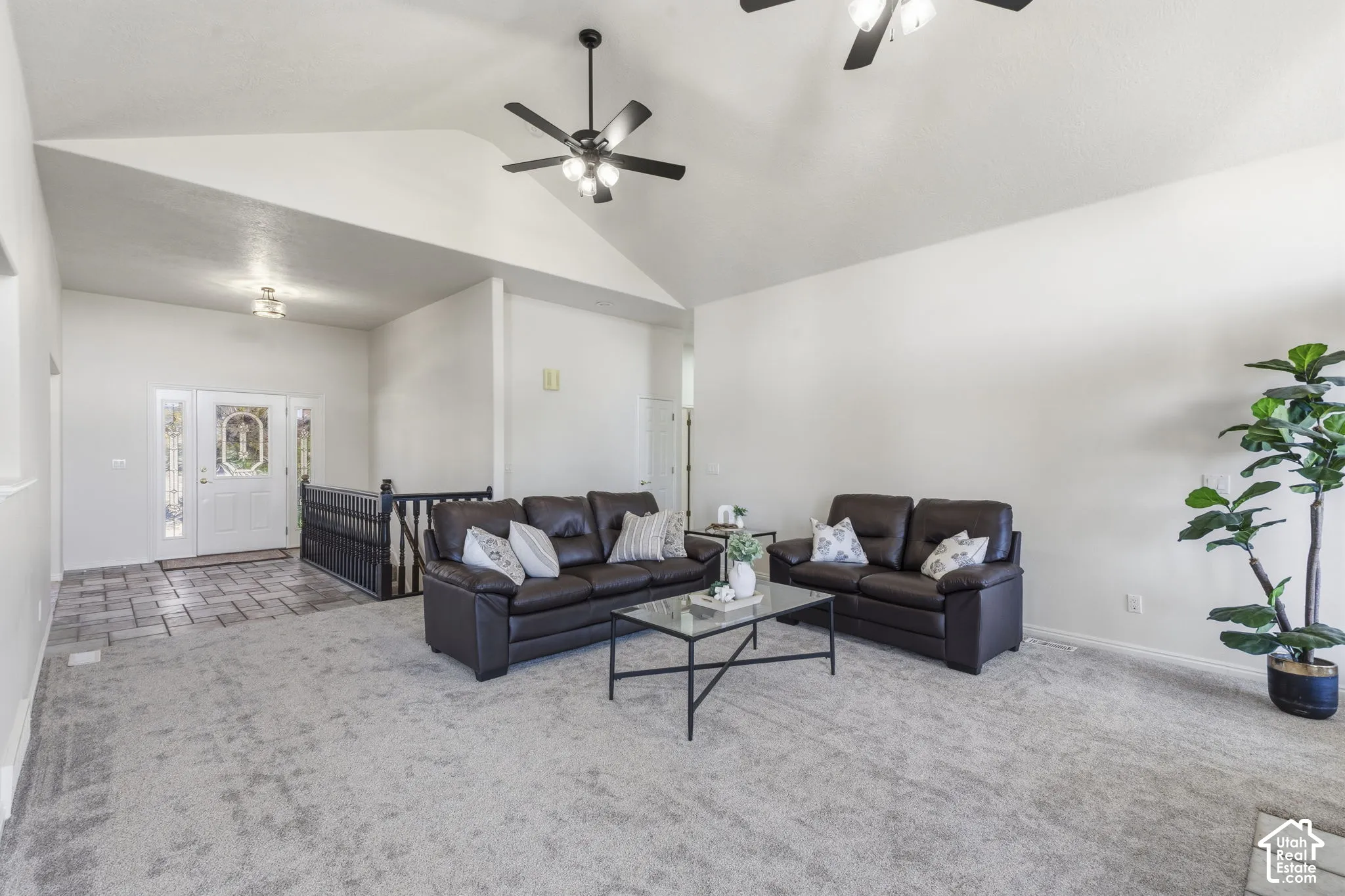 Vaulted ceilings, neutral carpeting, tiled entryway, wrought iron staircase railing, and dual ceiling fans